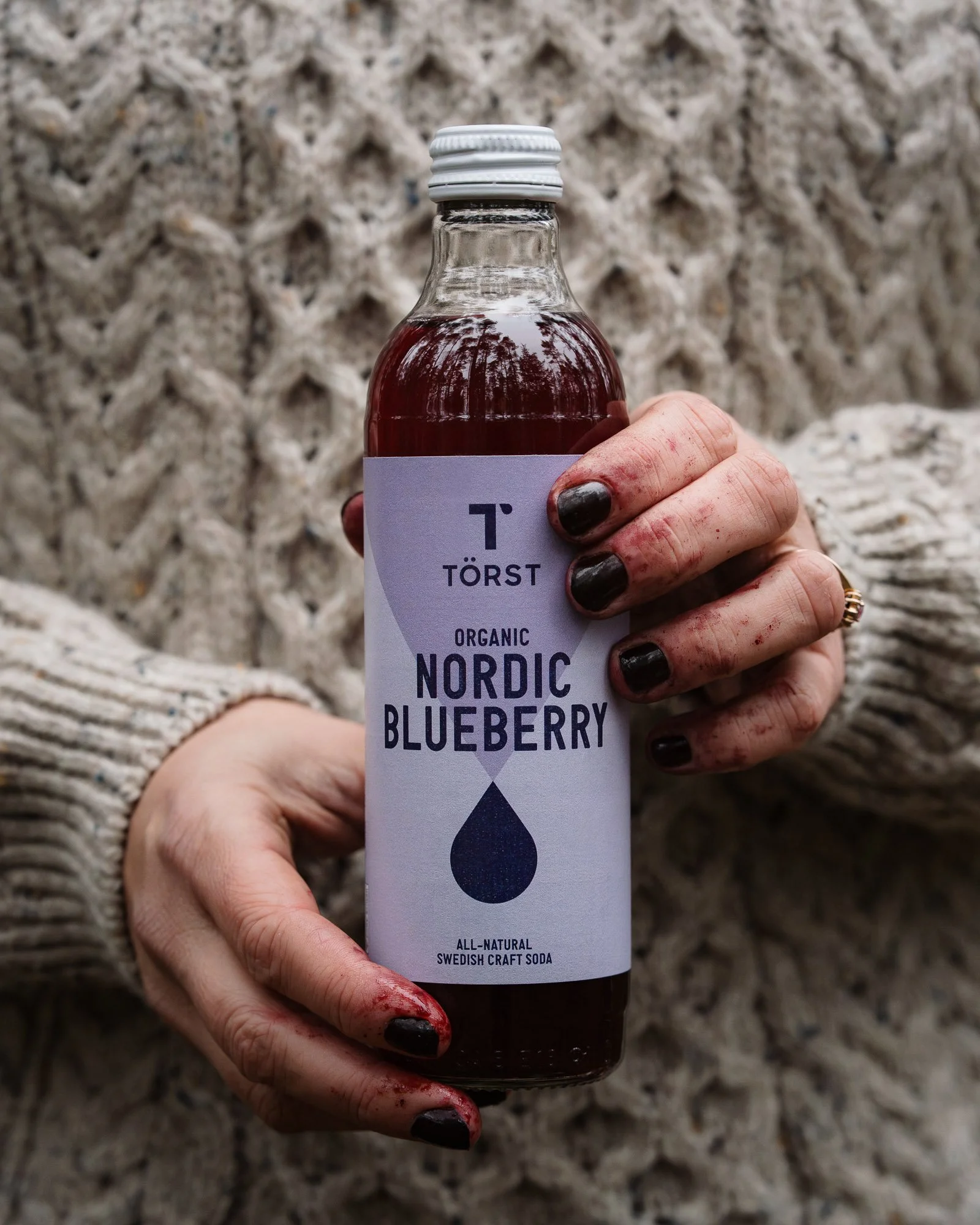 hands covered in blueberries holding a bottle of Törst Nordic Blueberry drink