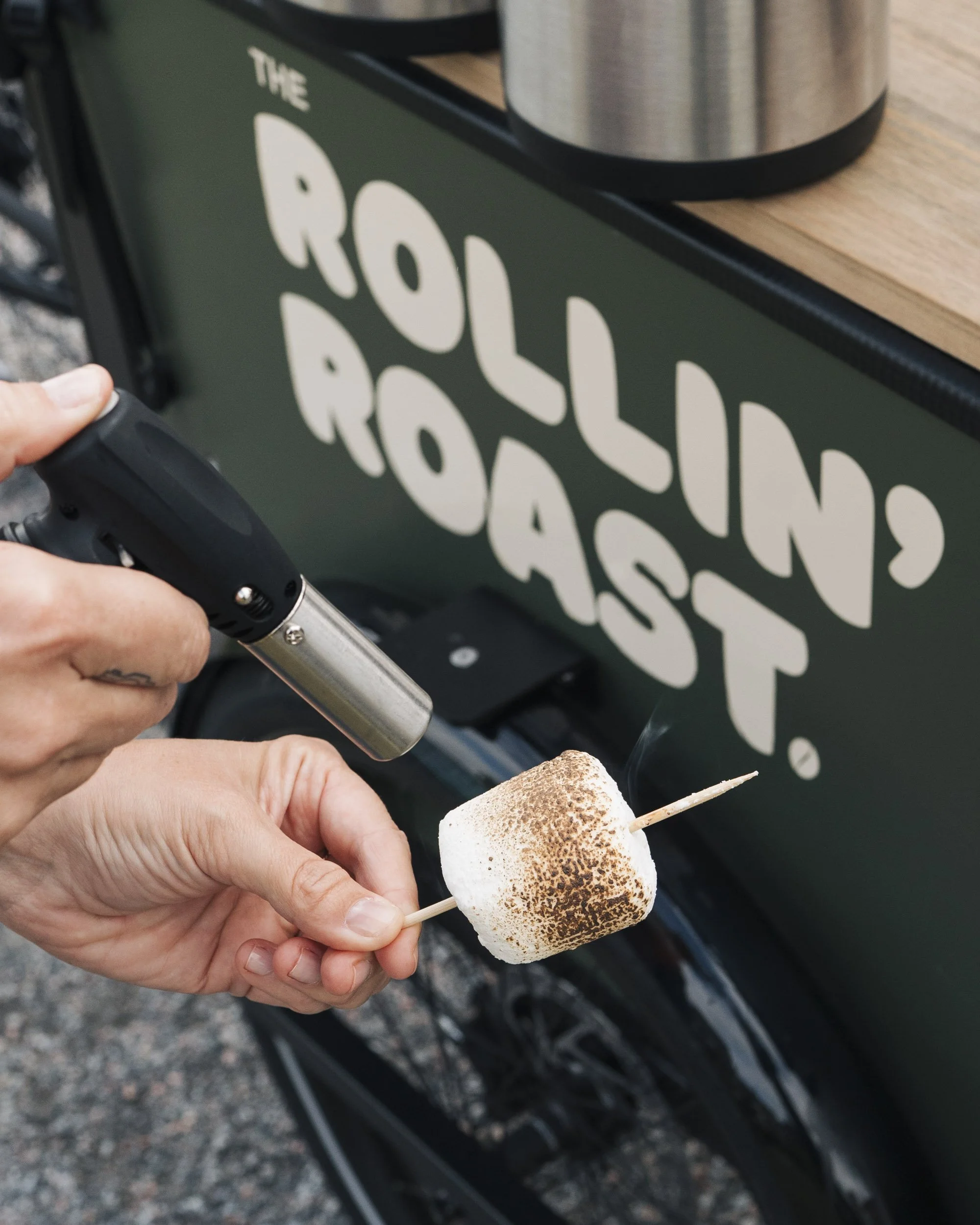Person holding a toasted marshmallow skewered on a stick with a grill in the background.