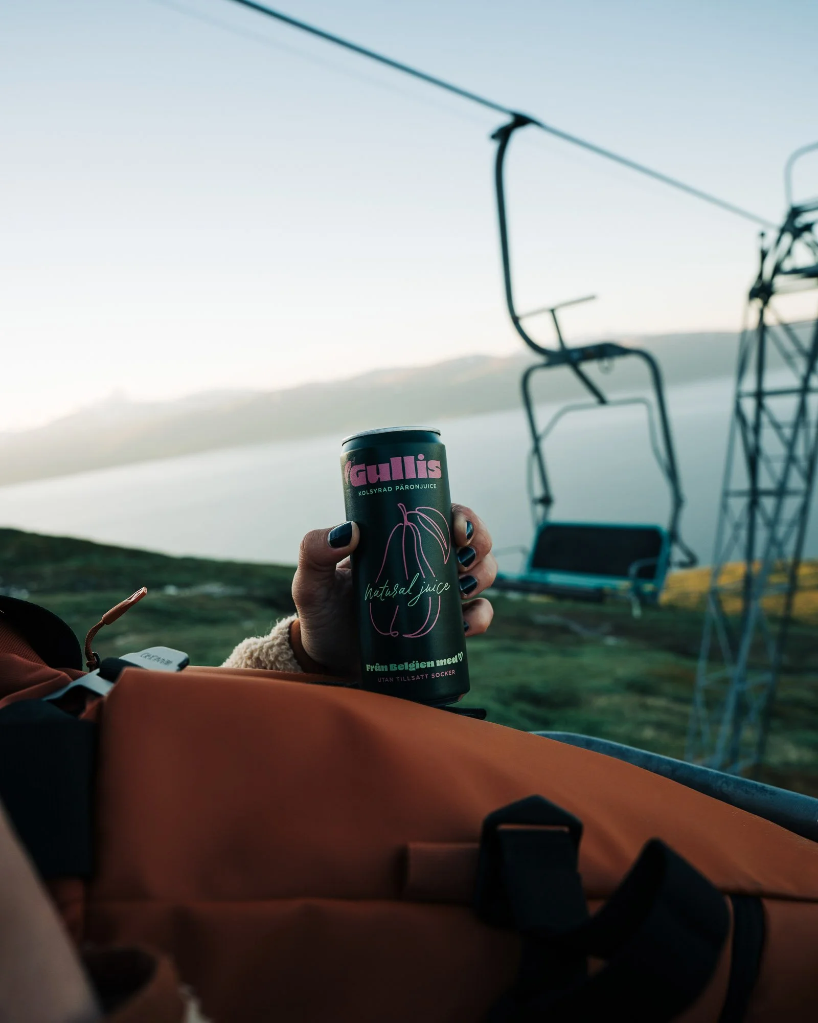 Person holding a can of Gullis natural juice with a background of a ski lift and a landscape with hills or mountains during daytime.