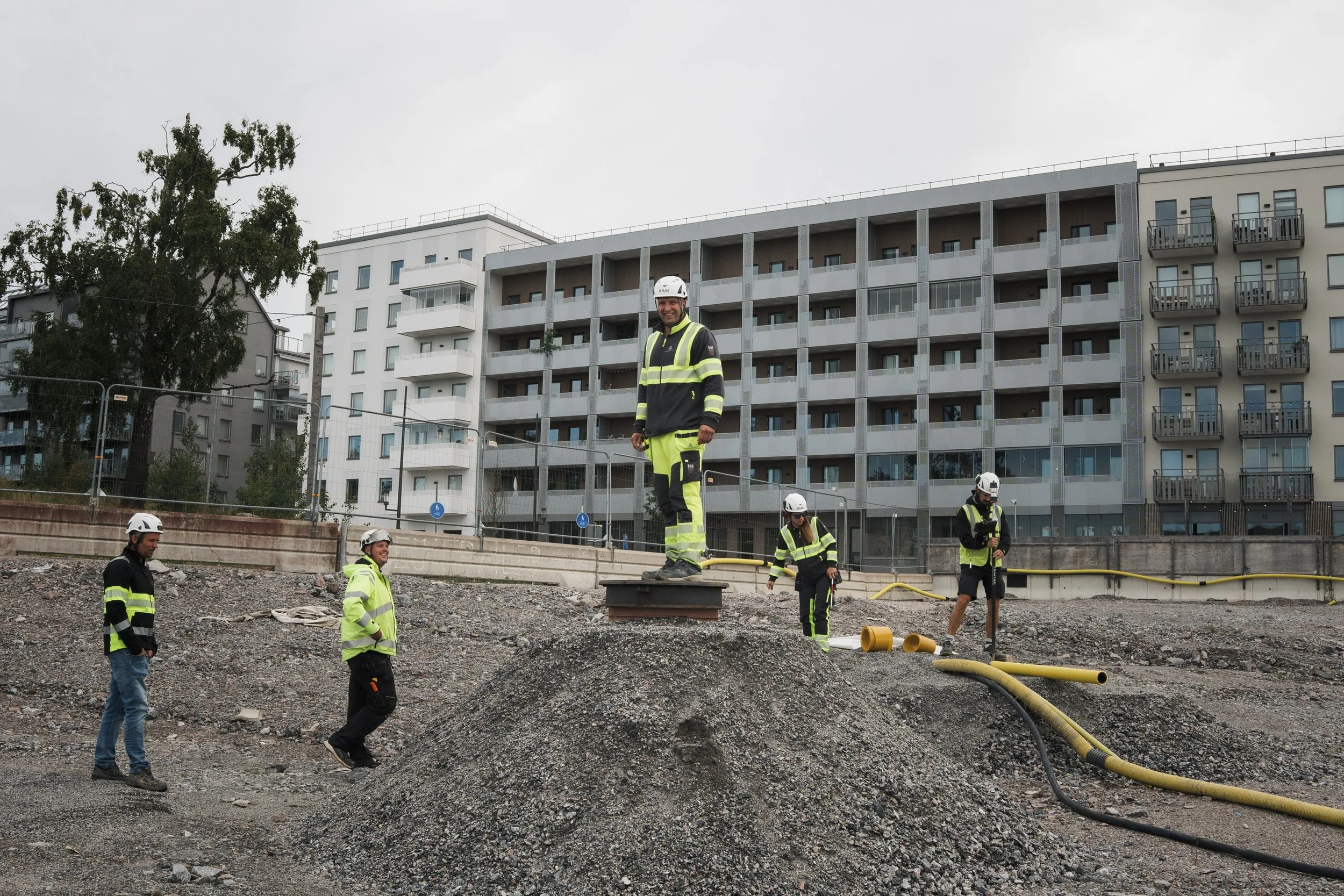Construction workers in safety gear working on an outdoor building site with apartment buildings in the background.