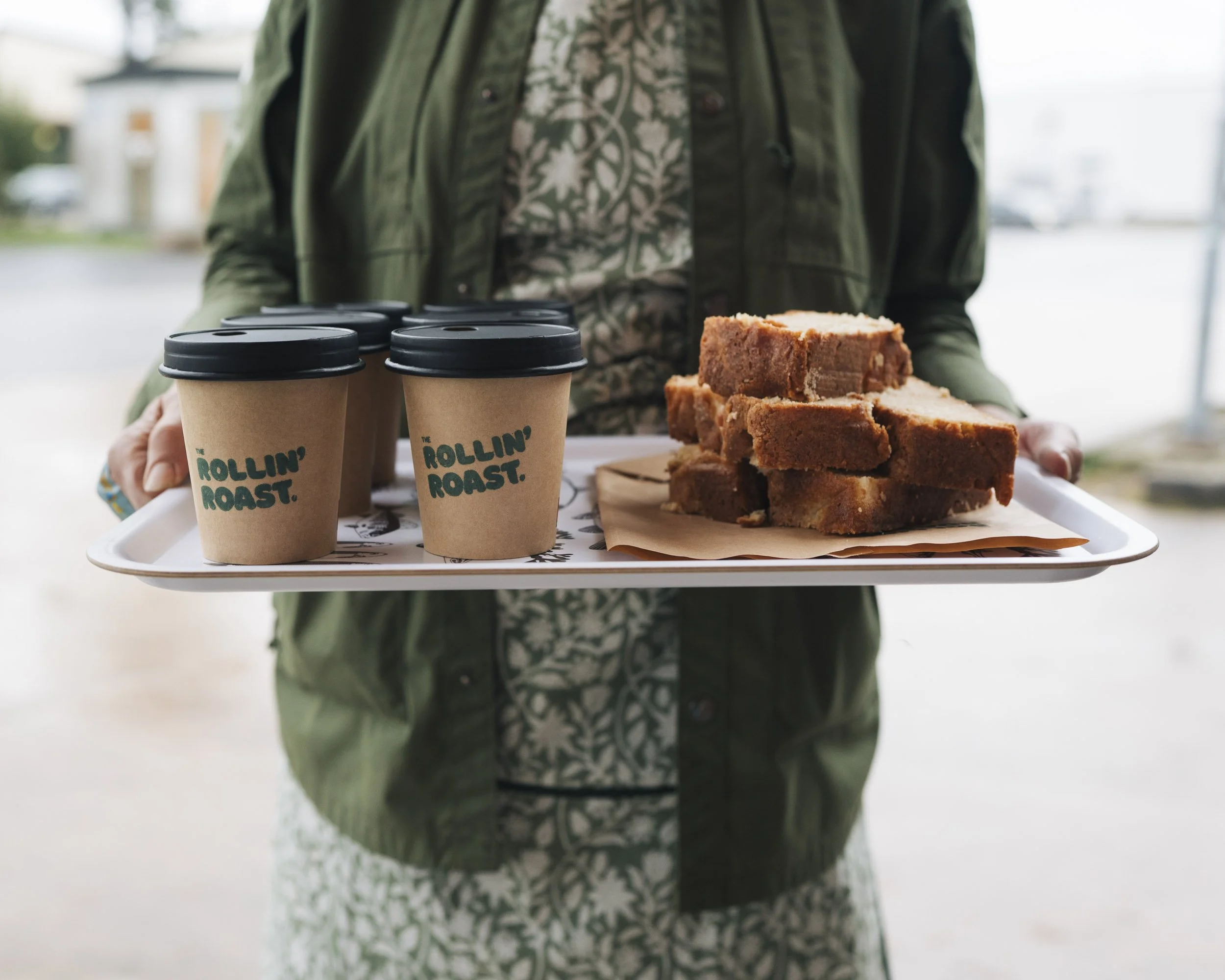 Person holding a tray with three cups of coffee and slices of cake.