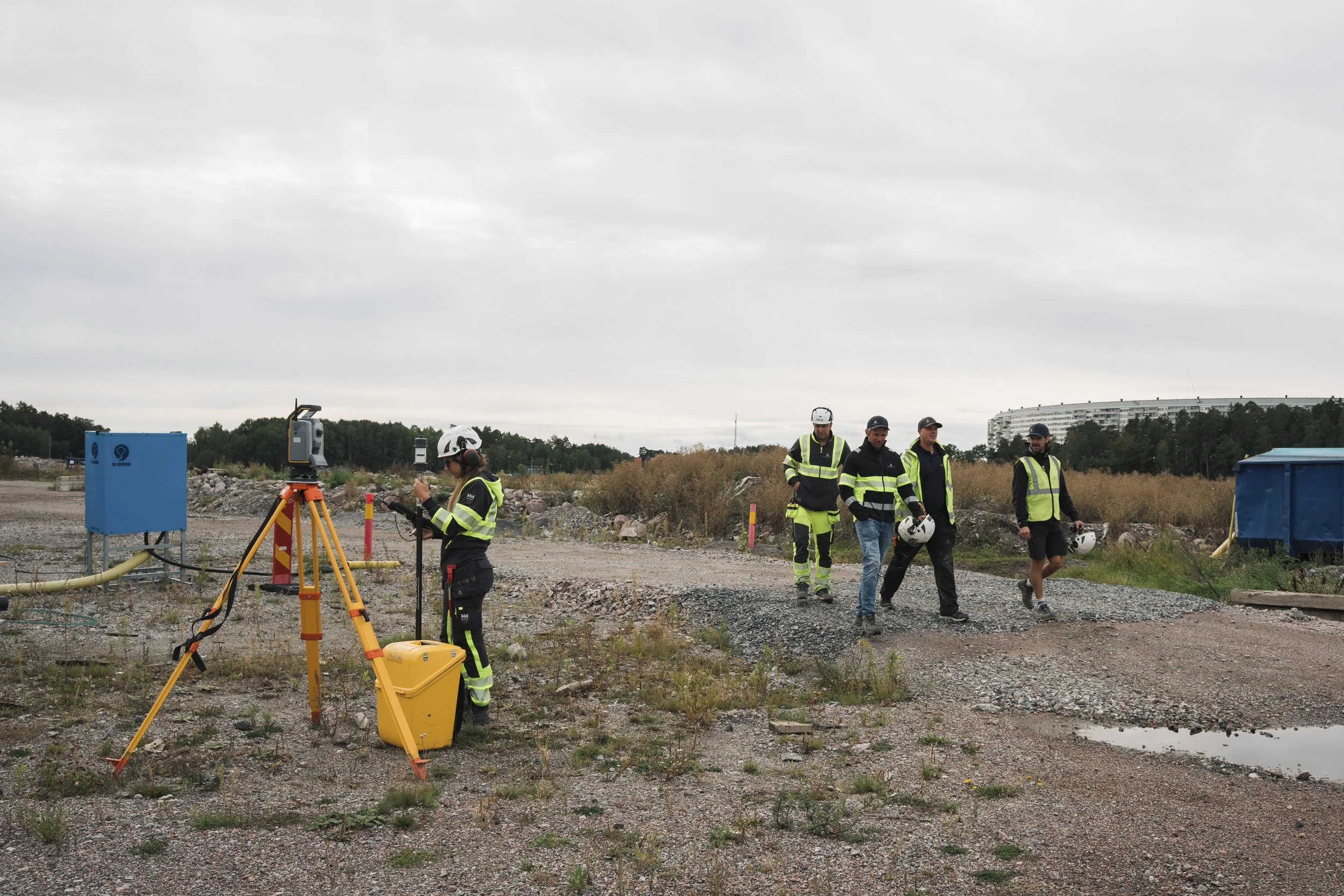 Construction workers at a site with surveying equipment on an overcast day.