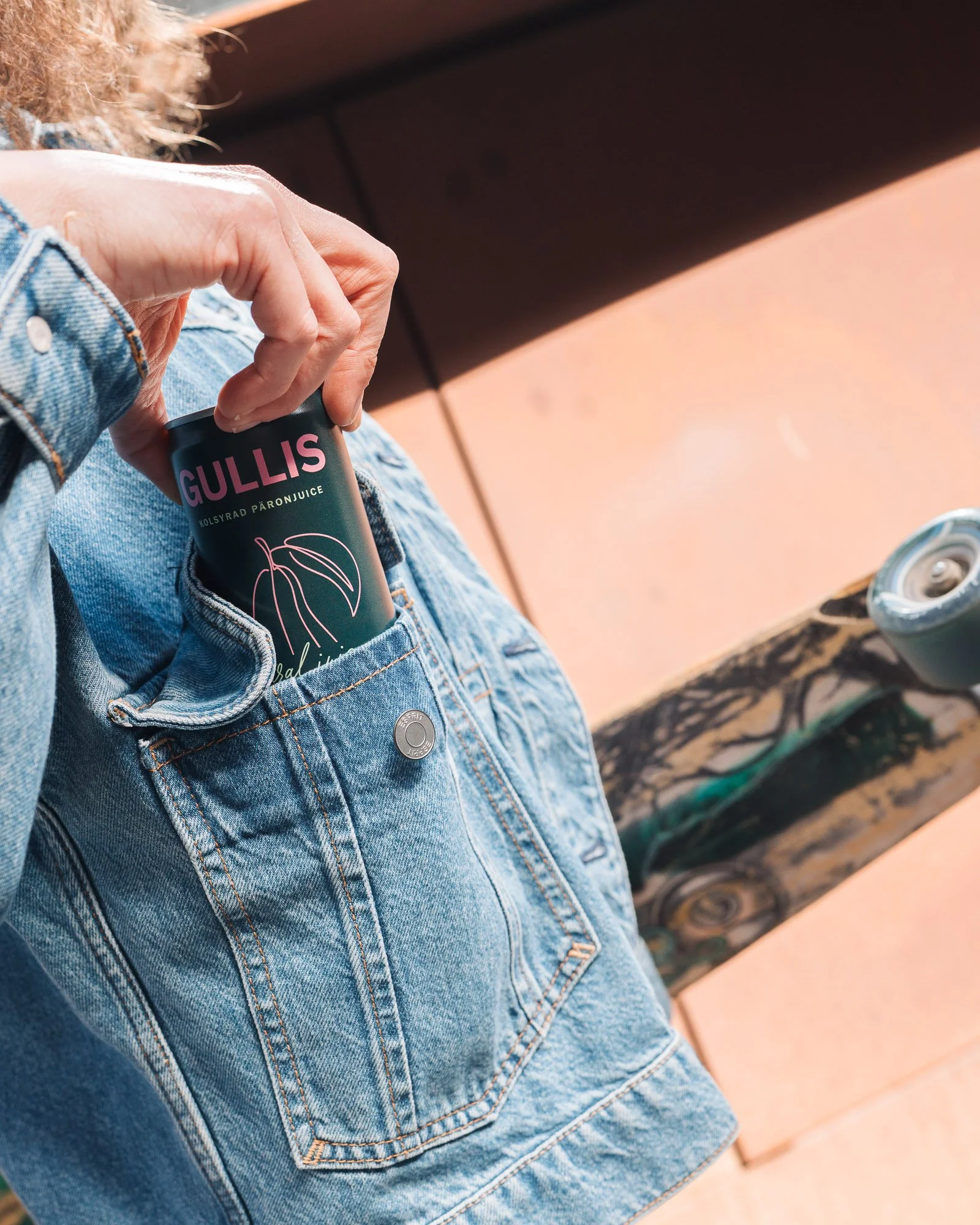 Person wearing a denim jacket and camouflage shorts holding a can of Gullís sparkling pomegranate juice