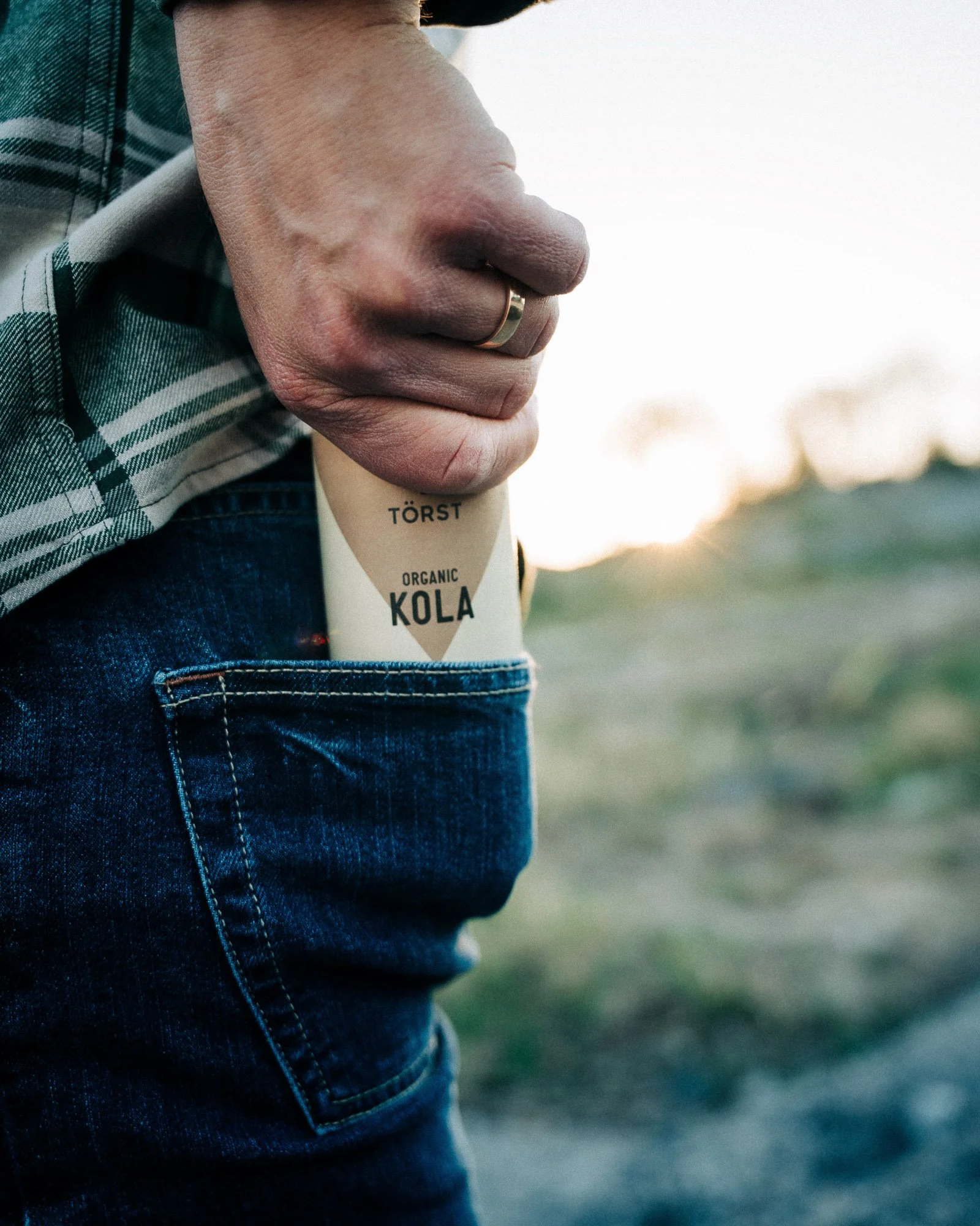 Close-up of a person's hand holding a bottle of organic Törst kola with a blurred outdoor background.