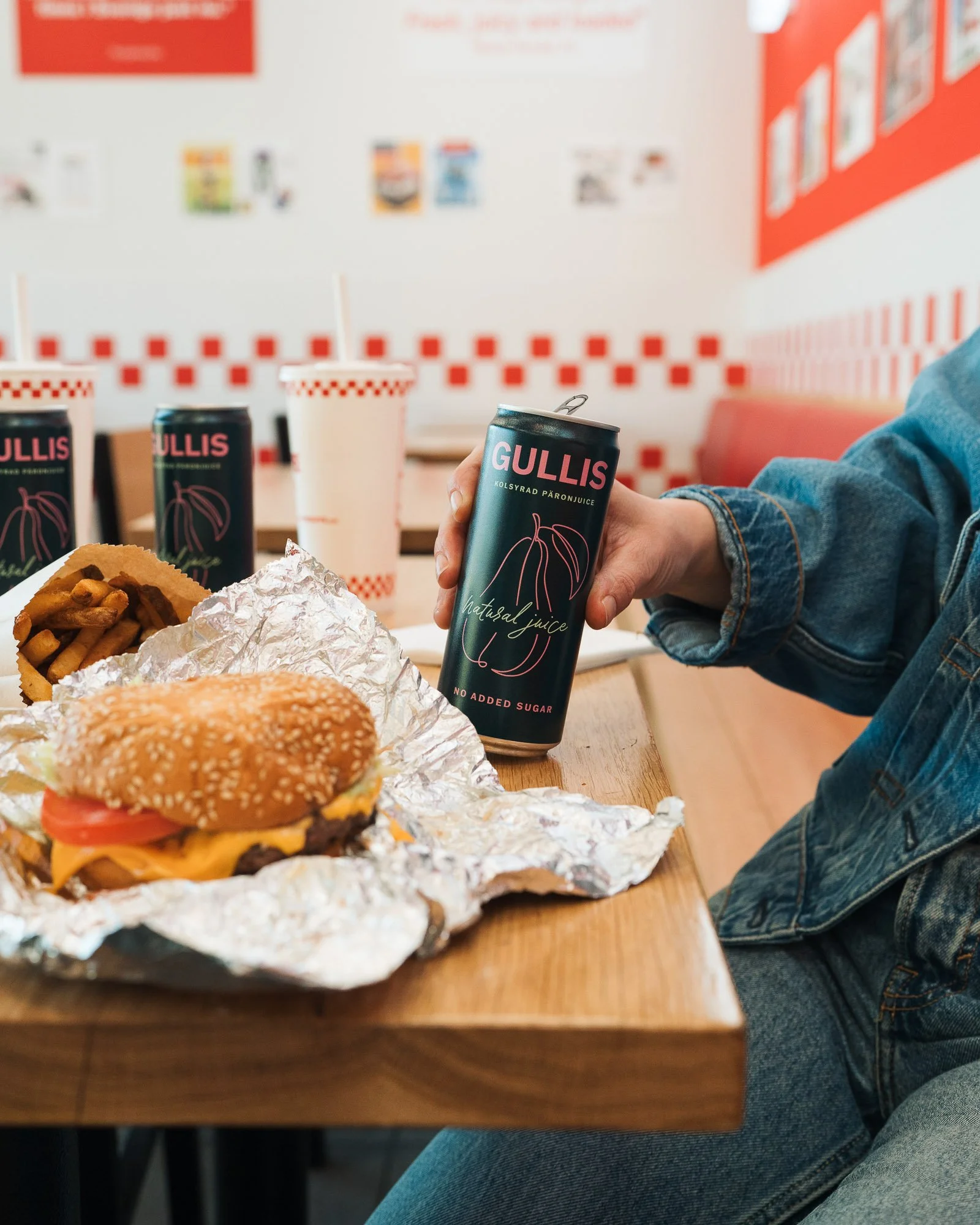 Fast food restaurant meal with a cheeseburger, fries, and a sandwich, along with a can of Gullis natural juice on a wooden table.