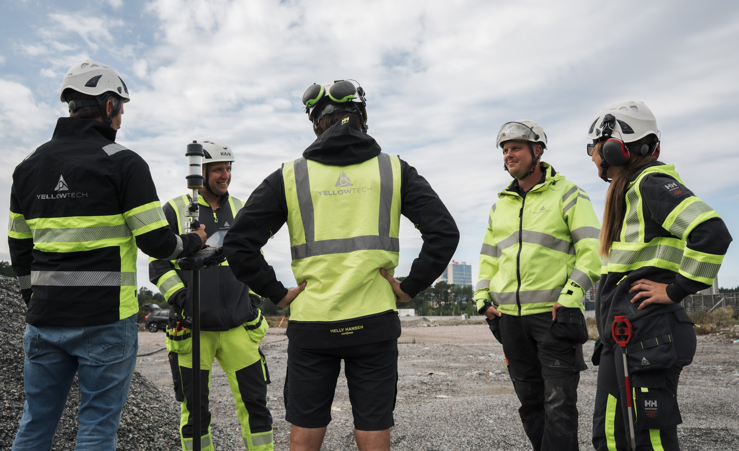 Group of five construction workers in safety gear, talking outdoors on a cloudy day at a construction site.