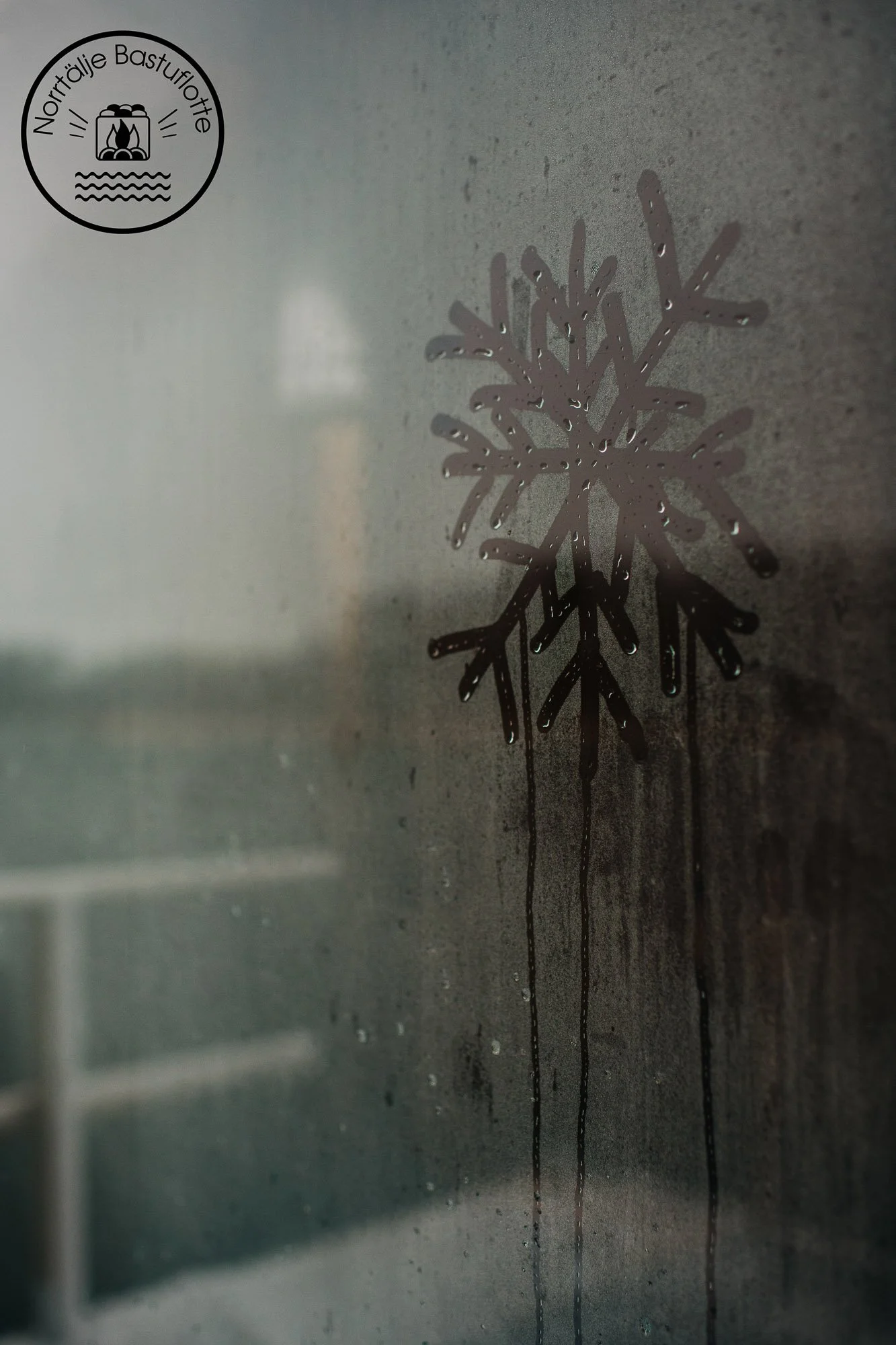 A snowflake-shaped sticker on a foggy window with water drips running down.
