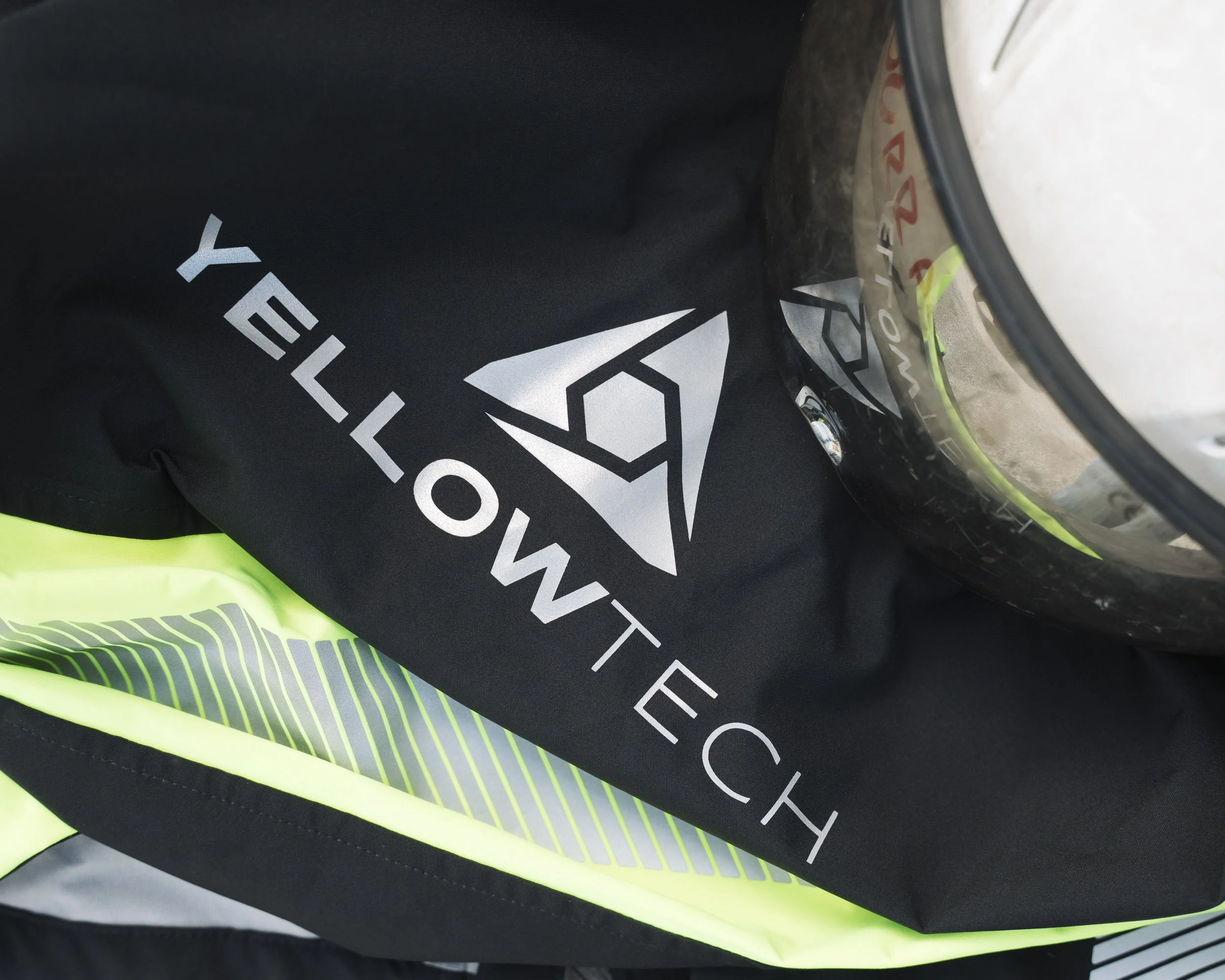 Close-up of a black object with the partially visible white text and logo, and a section of yellow safety vest underneath.