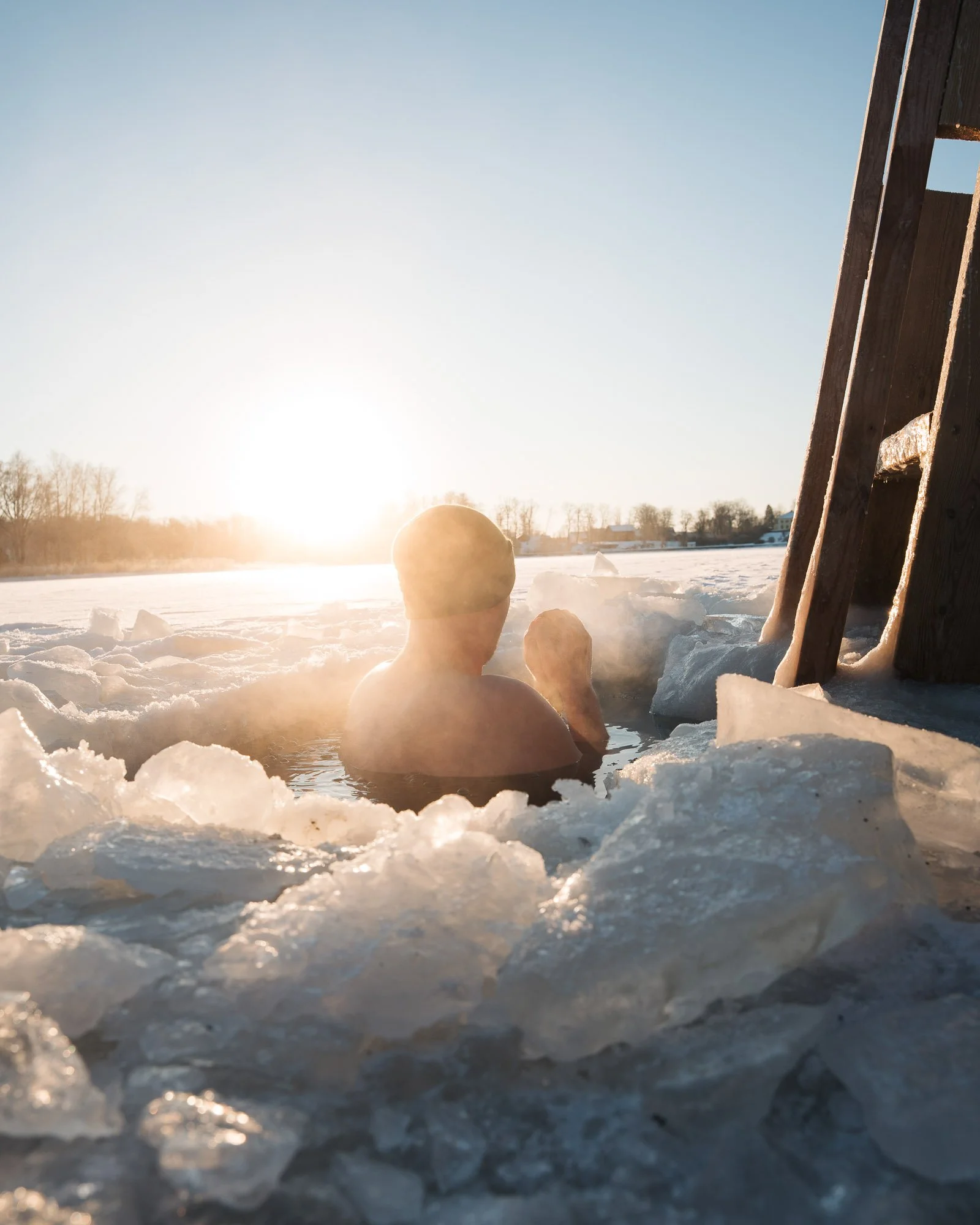 A frozen lake with ice and snow, a large snowball, smaller snowballs, a wooden structure, and the sun setting or rising in the background.