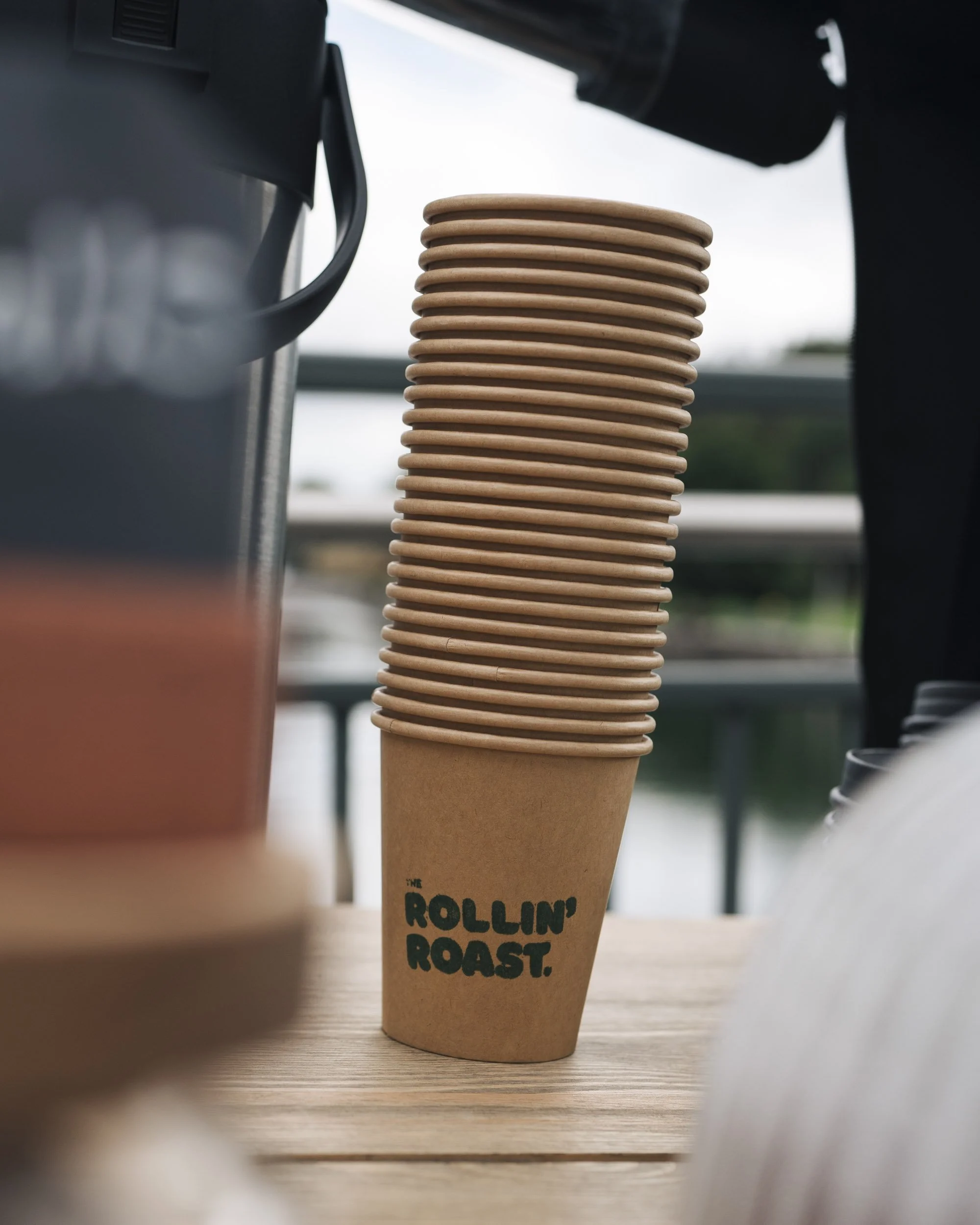 A stack of paper coffee cups with the text 'The Rollin' Doughnut' printed on the side, placed on a wooden table.