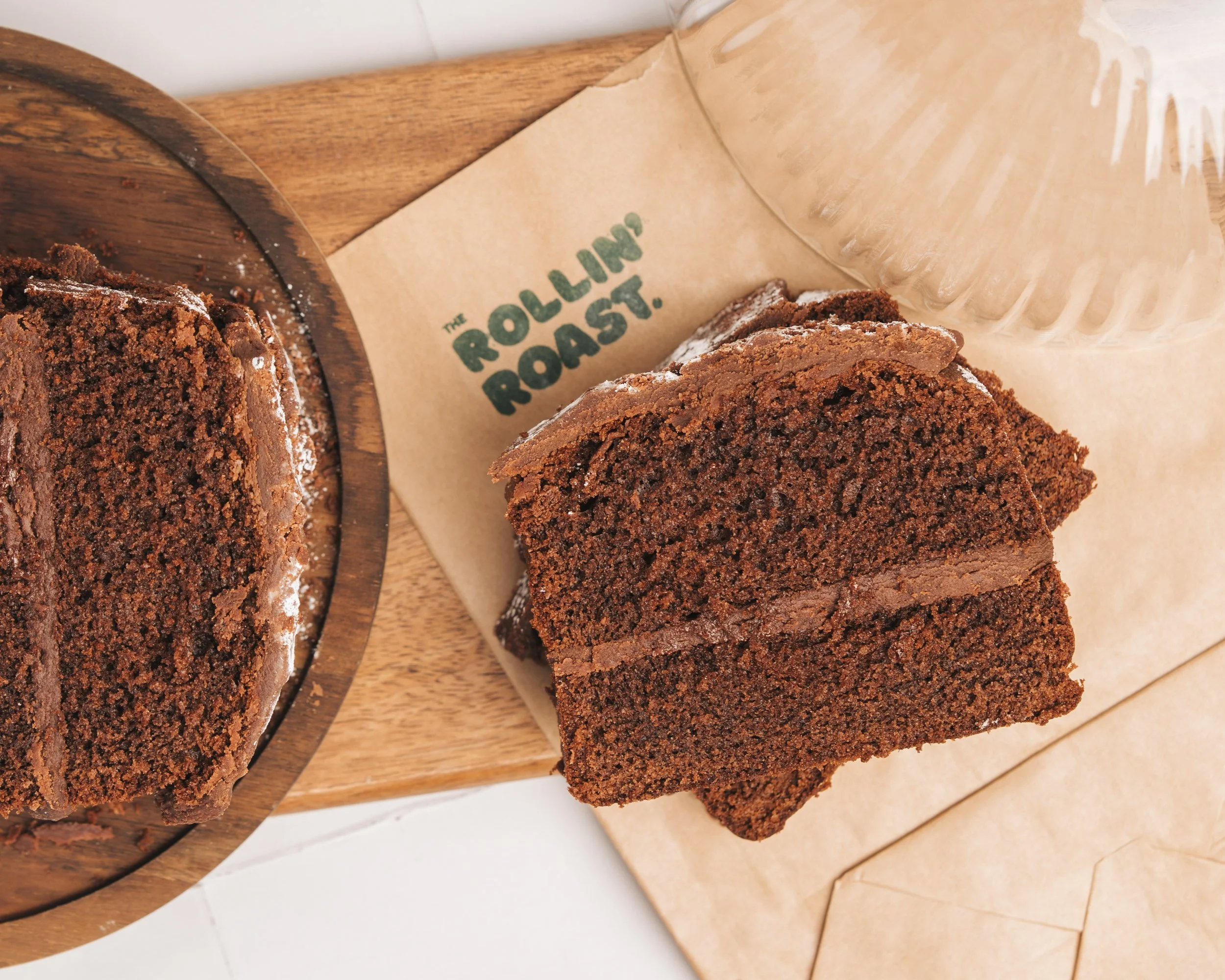 Slices of chocolate cake on a wooden cutting board with a paper bag that has "The Rocky Roast" written on it.