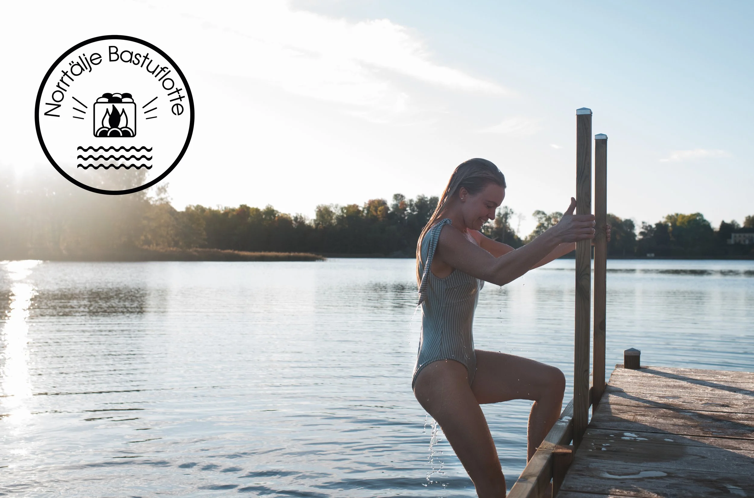 A woman in a swimsuit climbing out of a lake onto a wooden dock during sunset, with trees in the background and a logo in the top left corner that says "Nonträlje Bastu" with a camping stove and water waves.