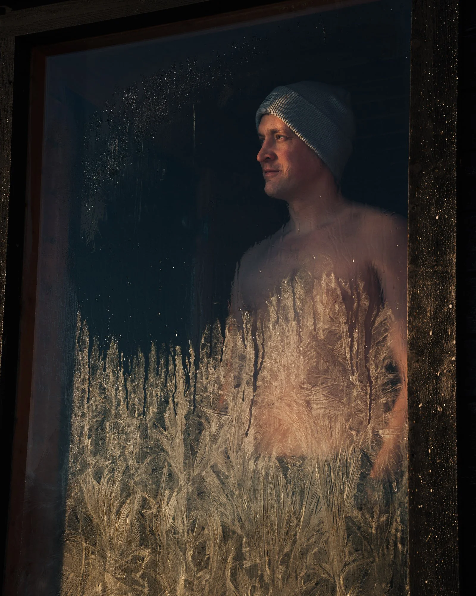 Man with gray beanie looking out a foggy window with frost patterns.