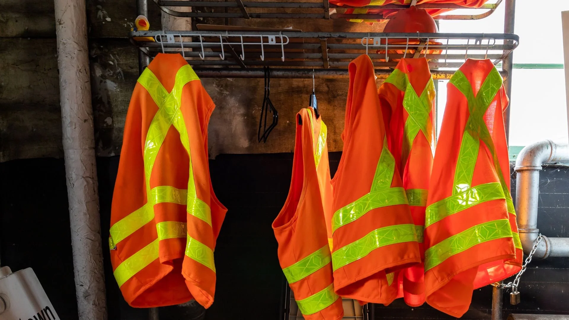 High-visibility orange safety vests hanging on a rack in a construction area.