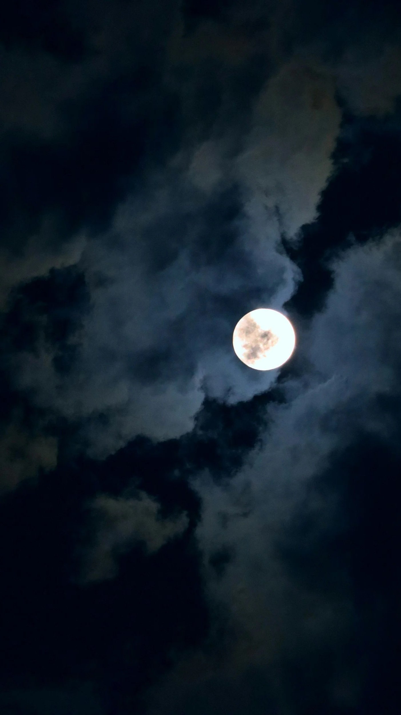 A bright full moon in the night sky partially obscured by dark clouds.