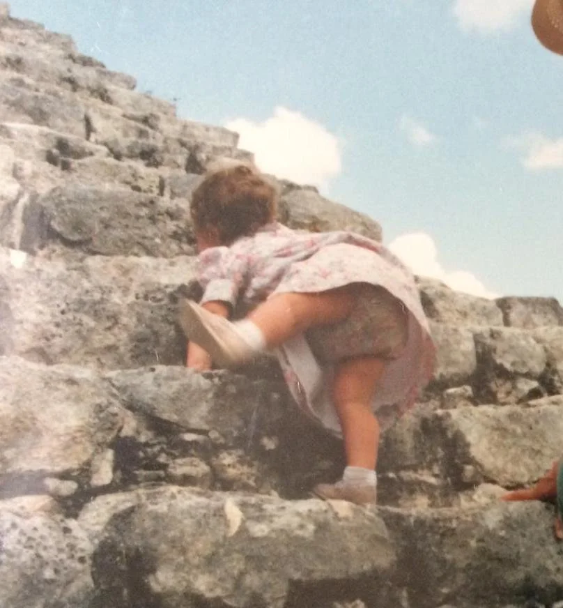 Child climbing a stone staircase outdoors on a partly cloudy day.