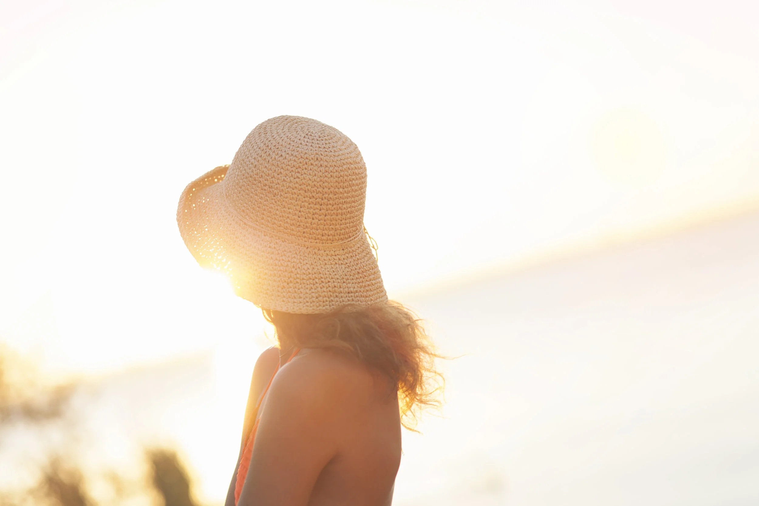Backlit portrait of woman wearing sun hat at sunset.