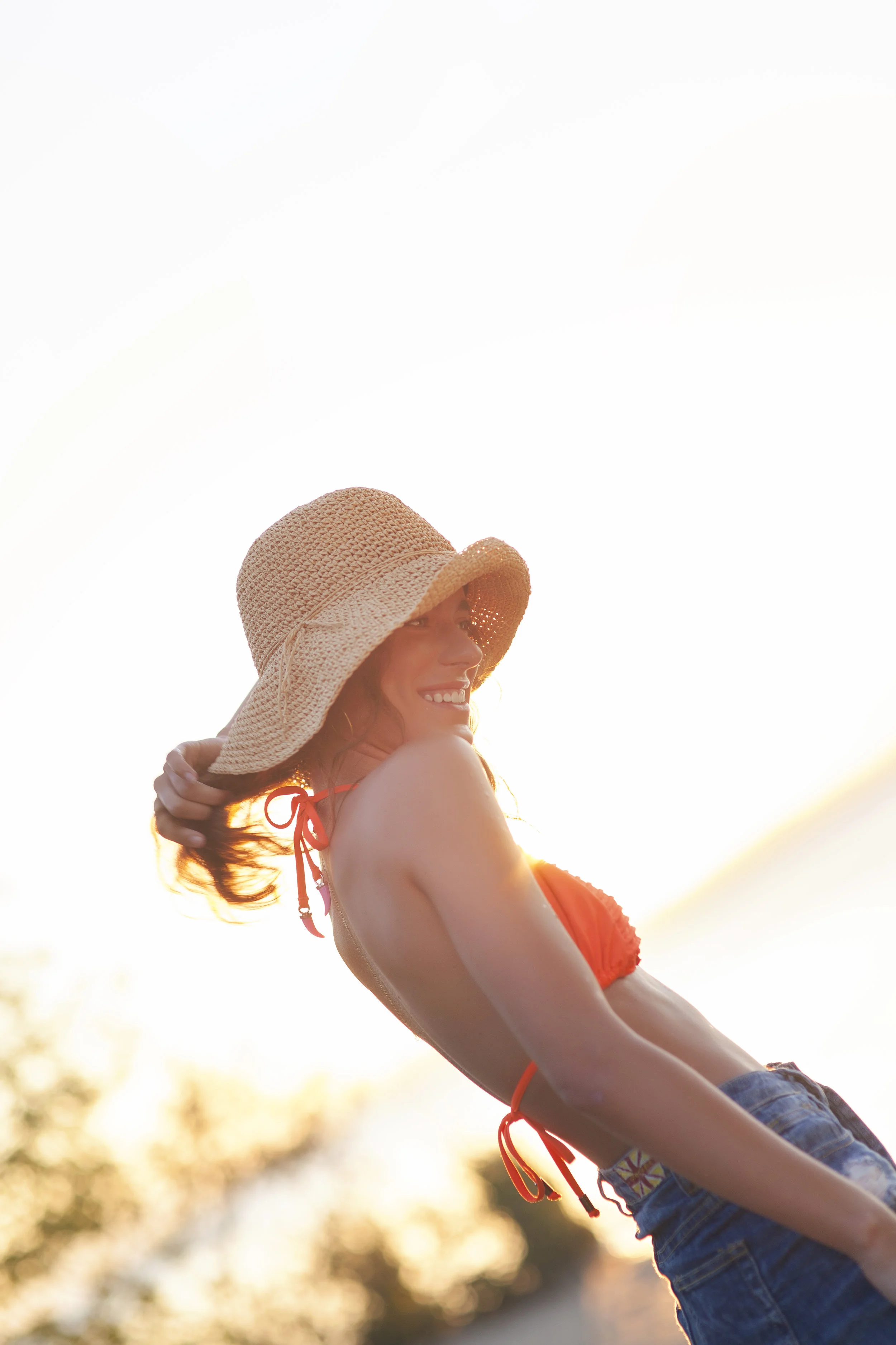 Backlit portrait of woman wearing sun hat.