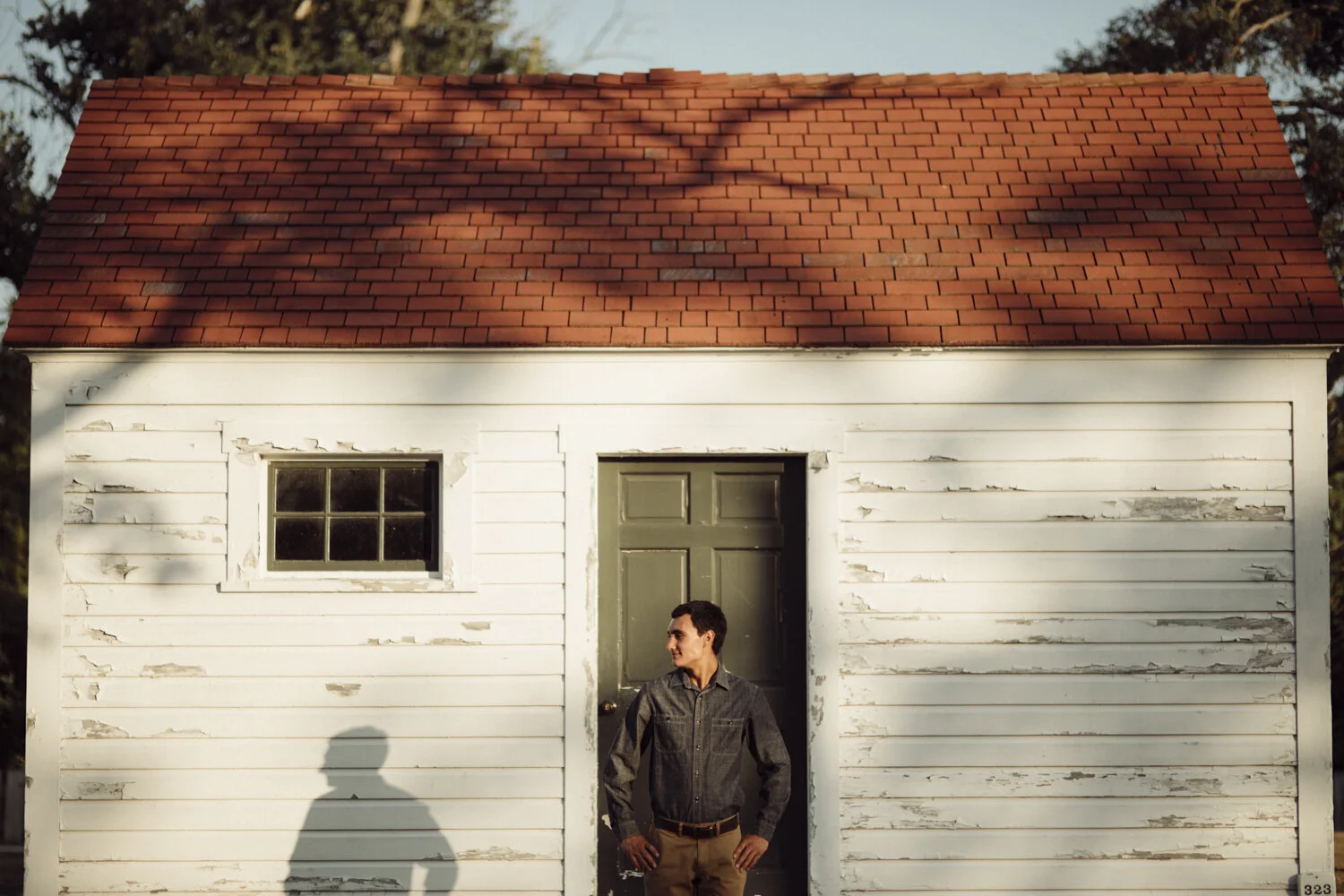 Environmental portrait of man standing outside historic farmhouse in Northern Michigan.