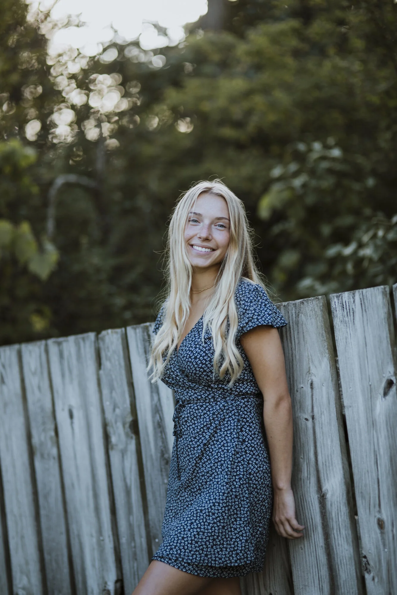 Environmental portrait of young woman by weathered fence.