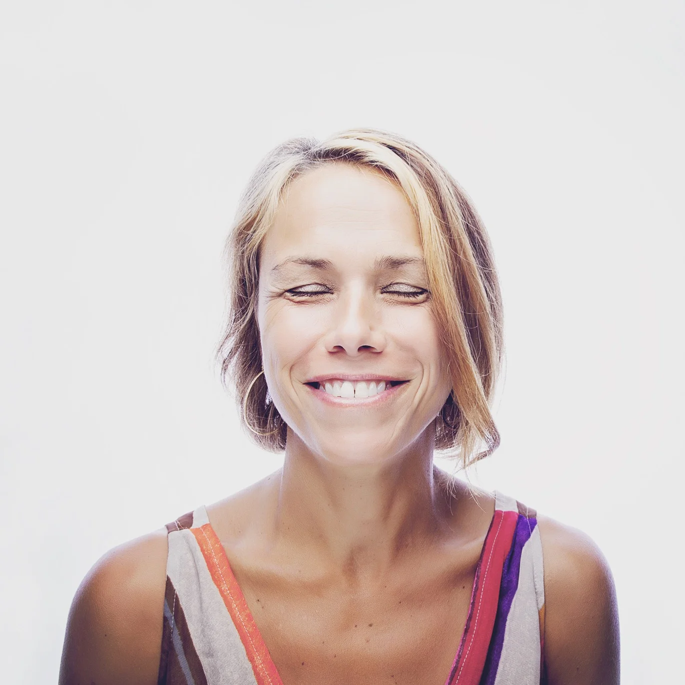 Natural light portrait of smiling woman with eyes closed.
