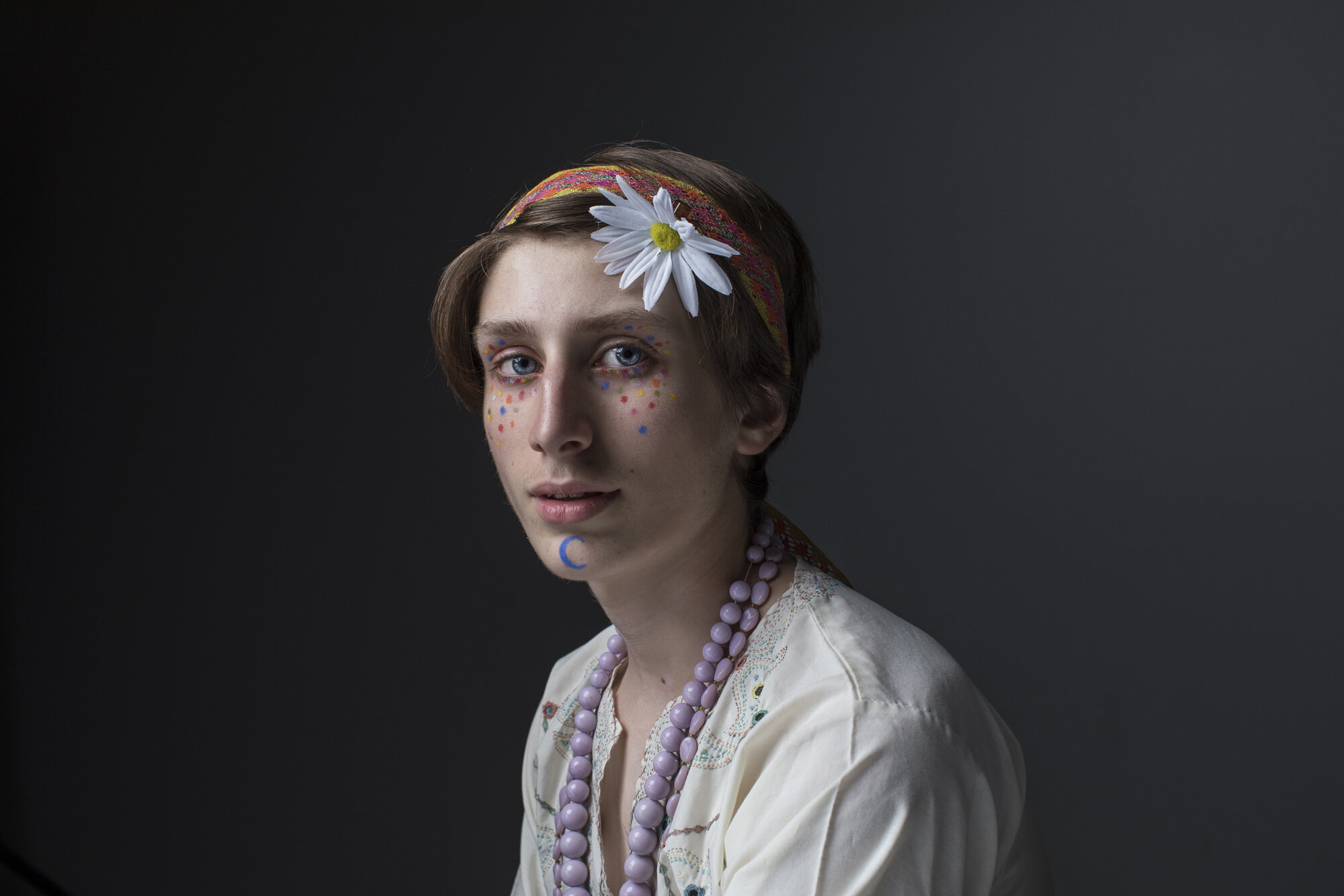 Creative portrait of young man with floral headpiece and painted freckles.