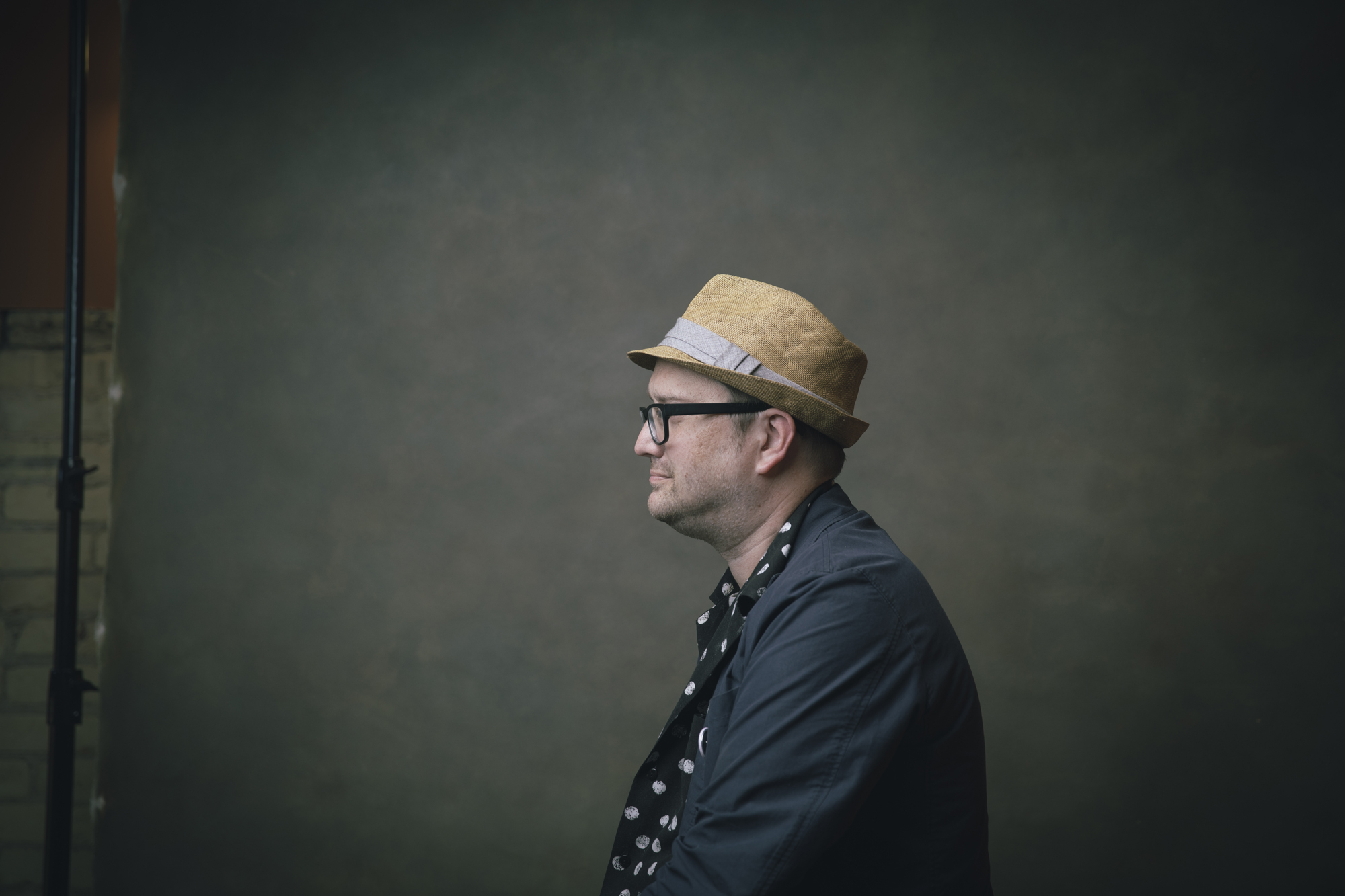 Editorial portrait of man in straw hat photographed in profile.