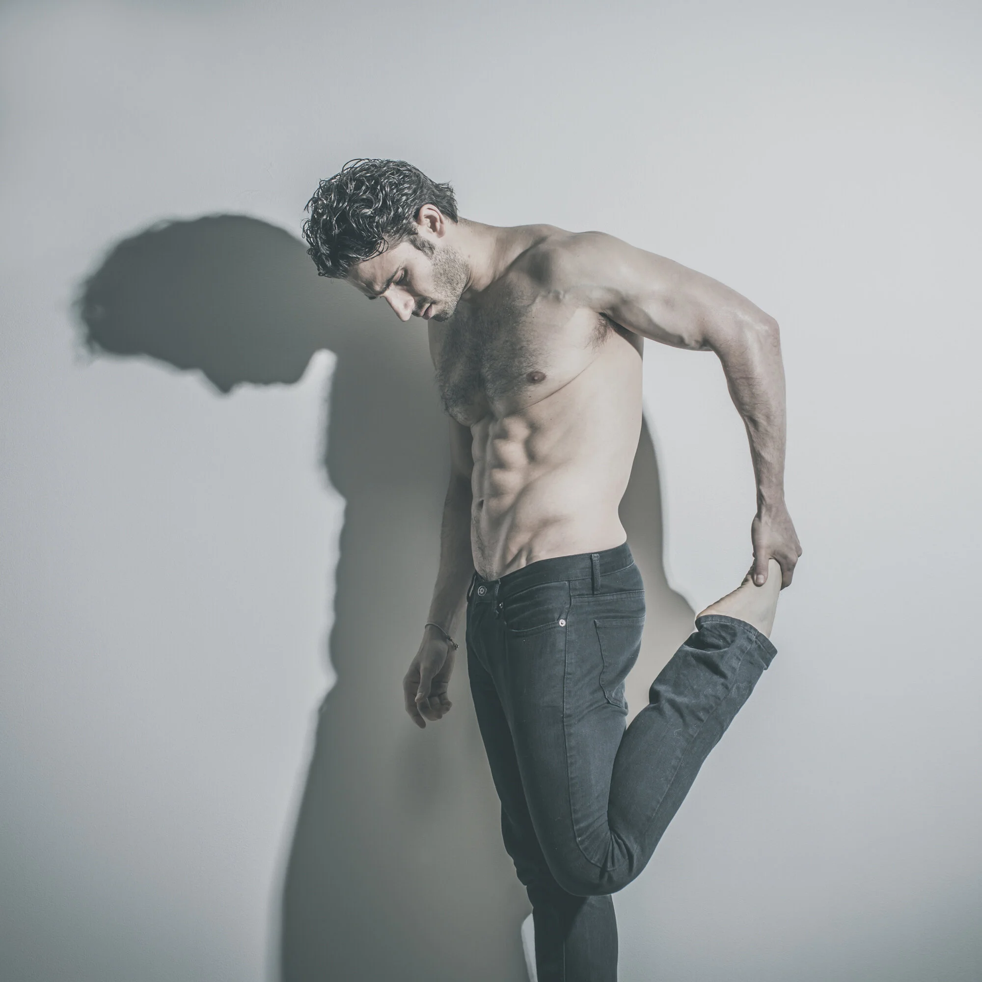 Editorial portrait of shirtless man with dramatic shadow.