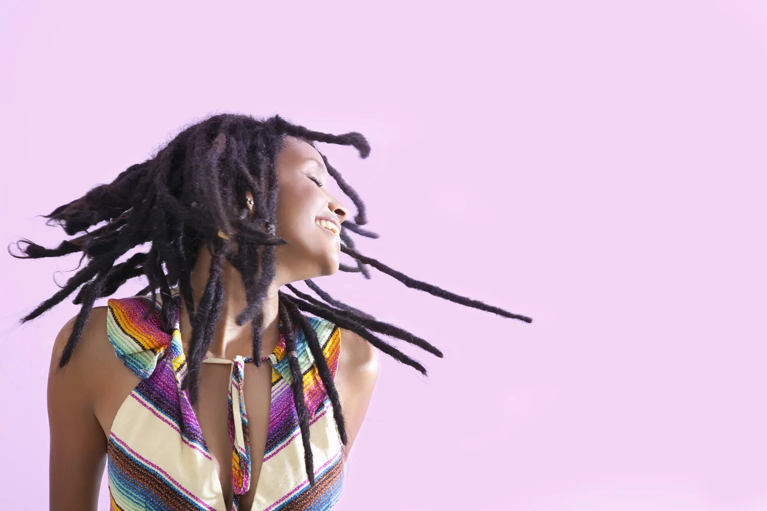 Editorial portrait of smiling woman with flowing dreadlocks against pink background.