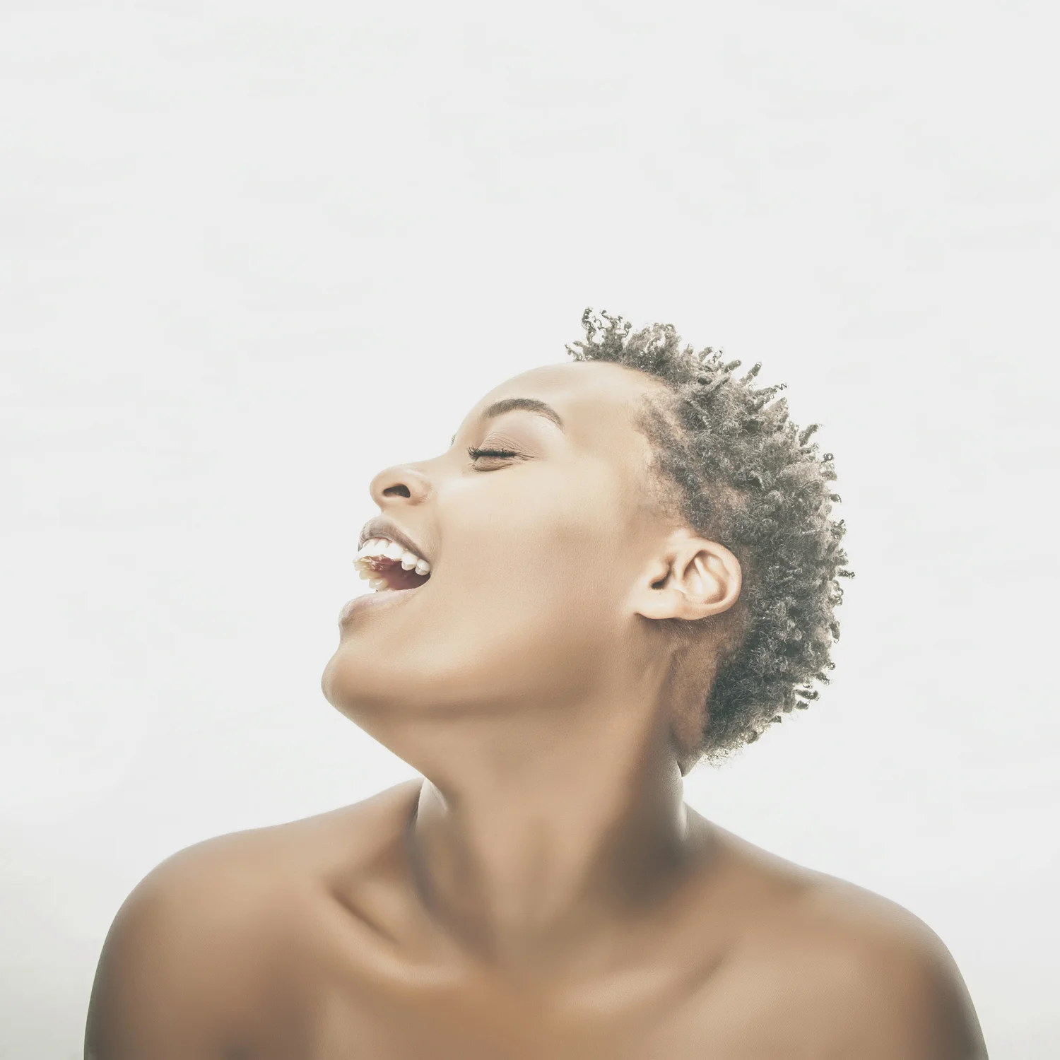 High-key studio portrait of smiling woman with eyes closed.