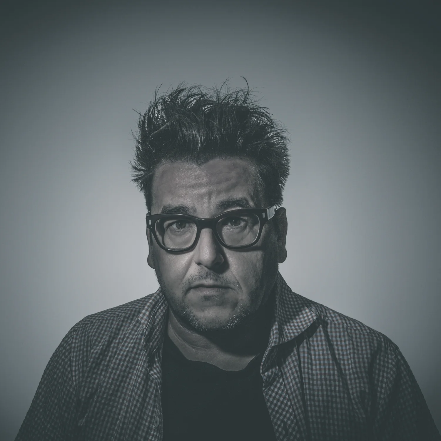 Studio portrait of man wearing glasses against dark background.