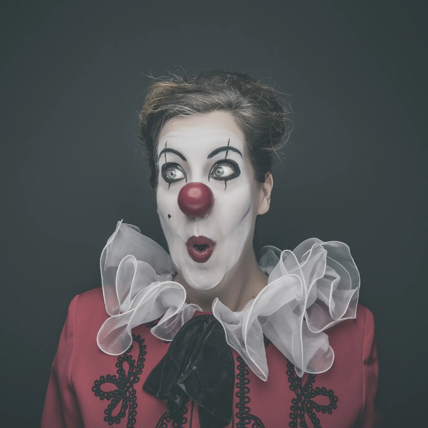 Creative studio portrait of woman dressed as a clown with theatrical makeup.
