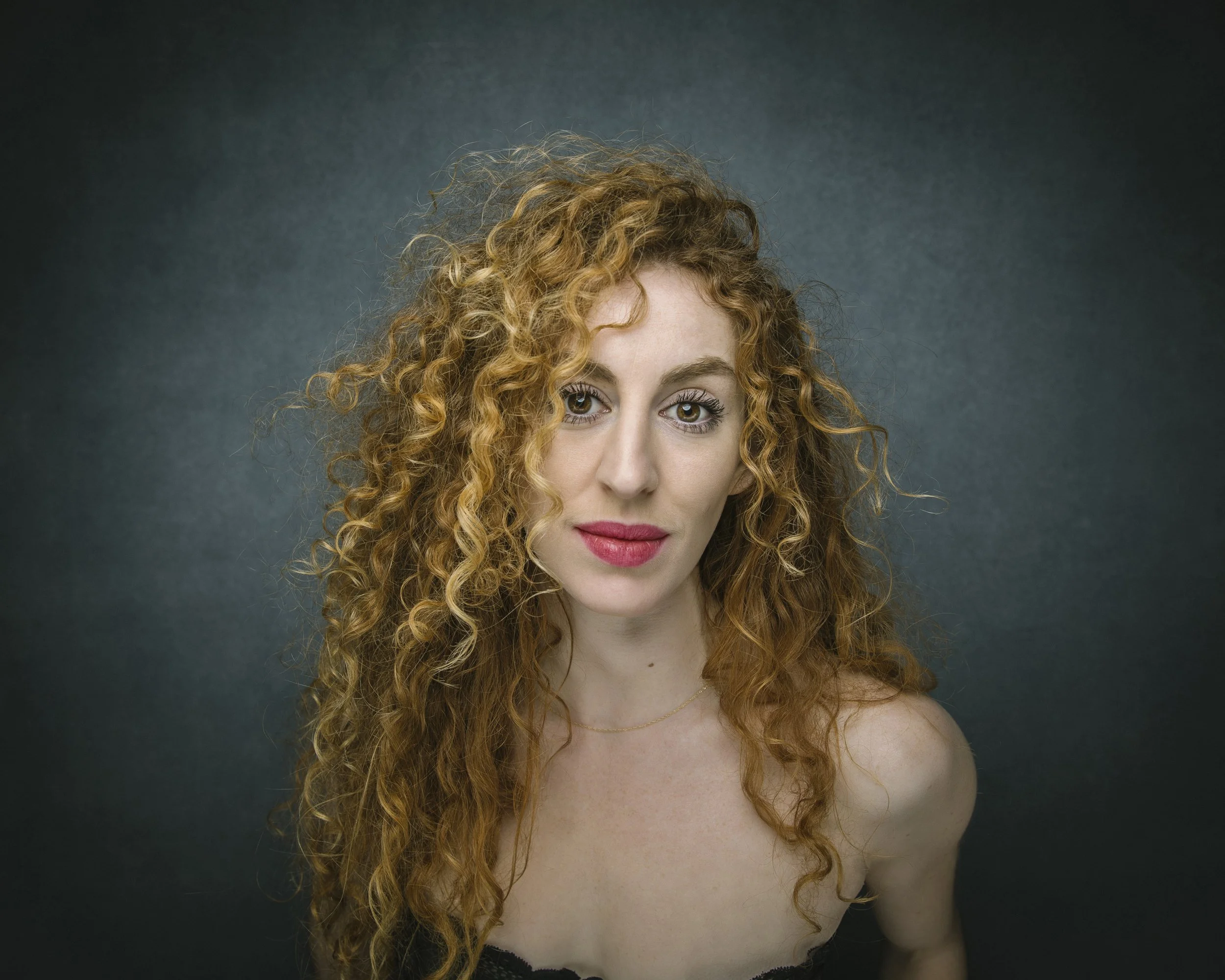 Studio portrait of red-haired woman with curly hair.