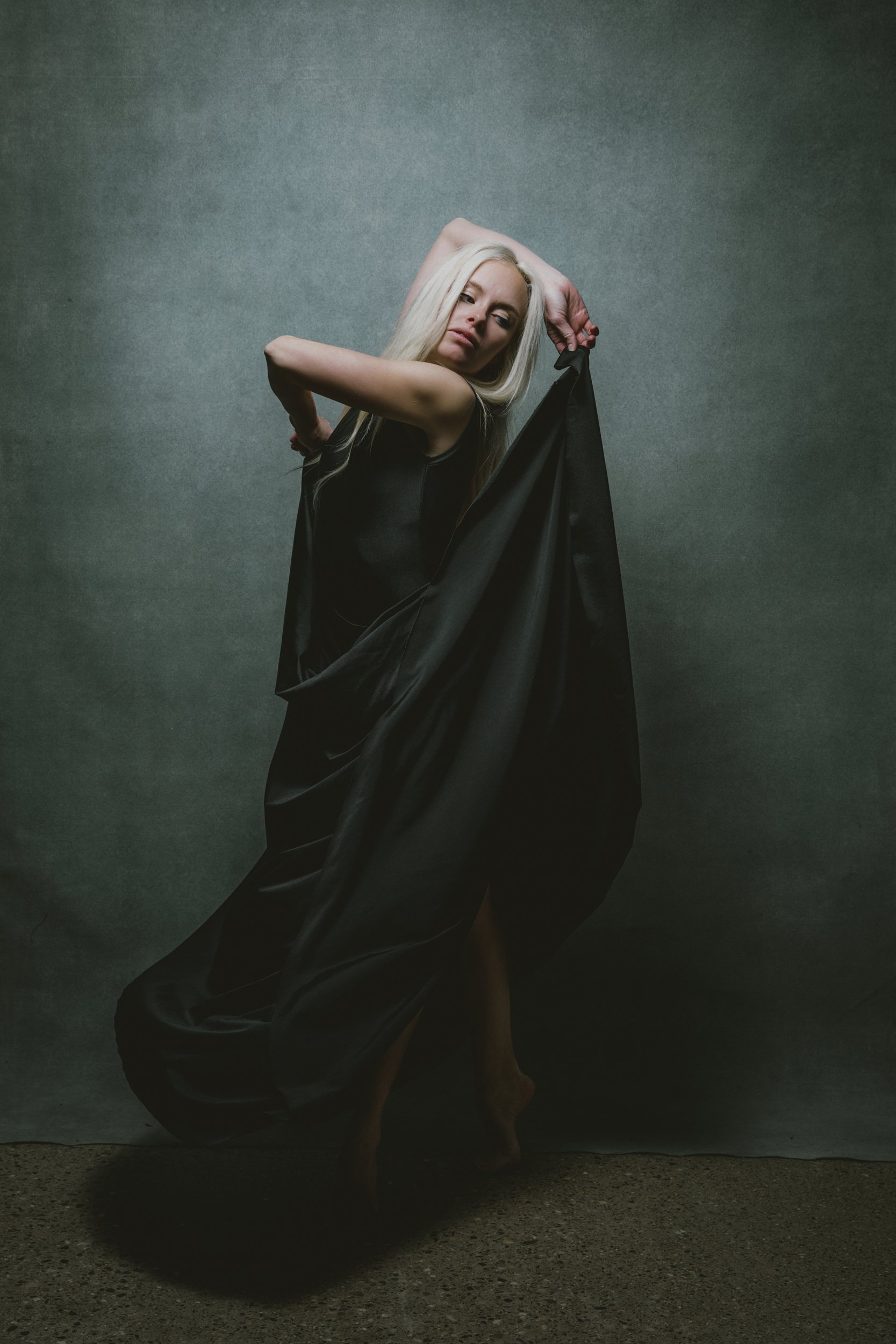 Editorial portrait of woman with platinum blonde hair draped in flowing black fabric.