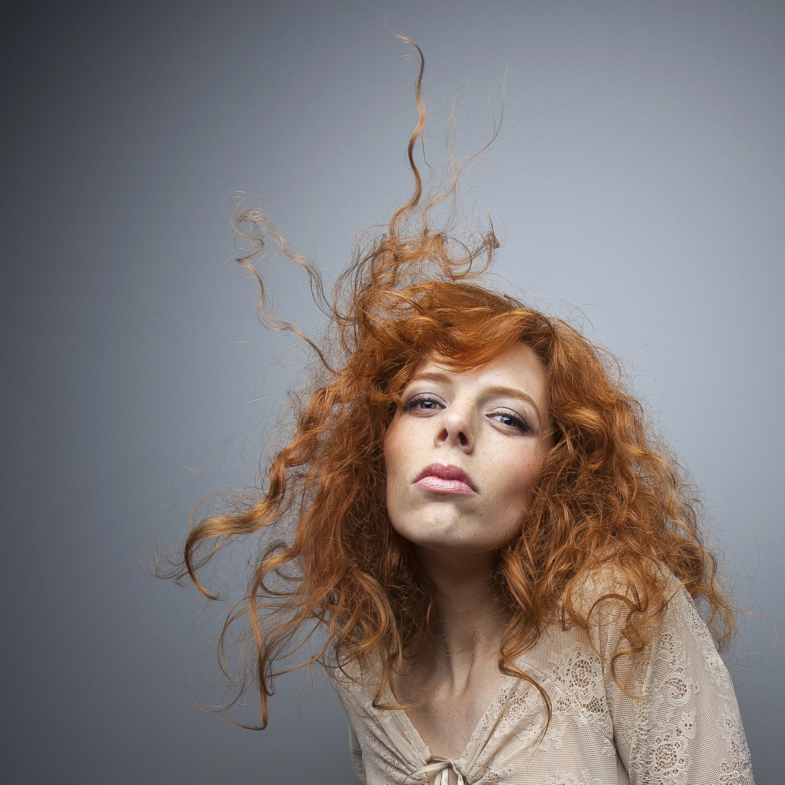 Editorial portrait of red-haired woman with windblown hair.