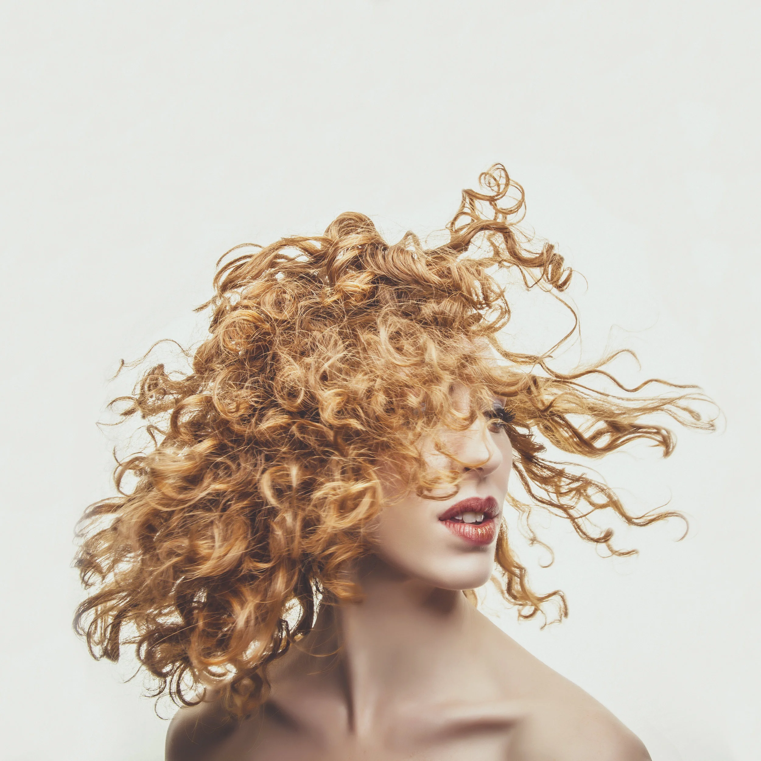 Beauty portrait of woman with windblown curly hair in natural light.