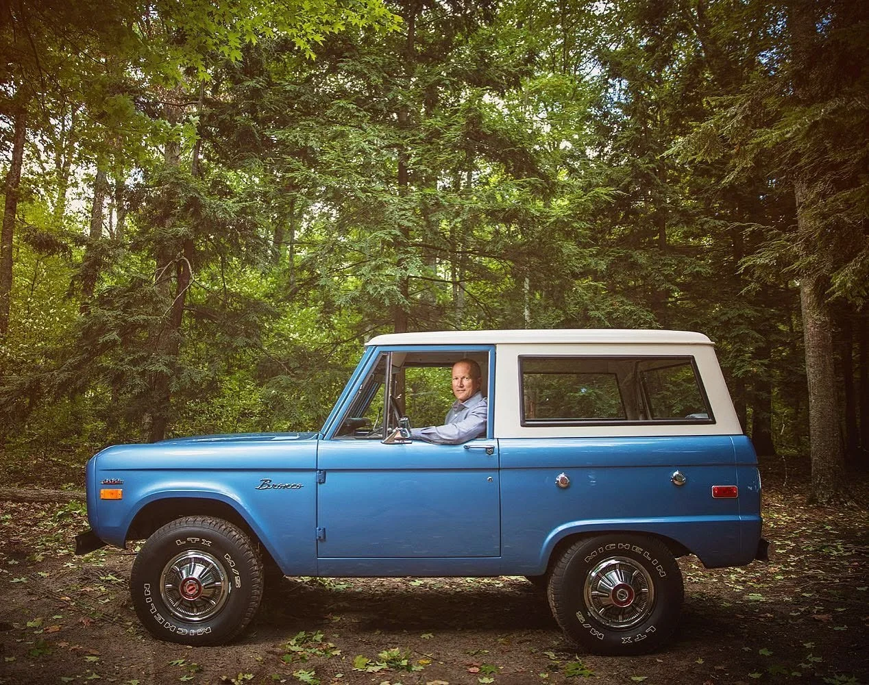 Environmental portrait of McKeel Hagerty inside vintage Ford Bronco in Northern Michigan forest.