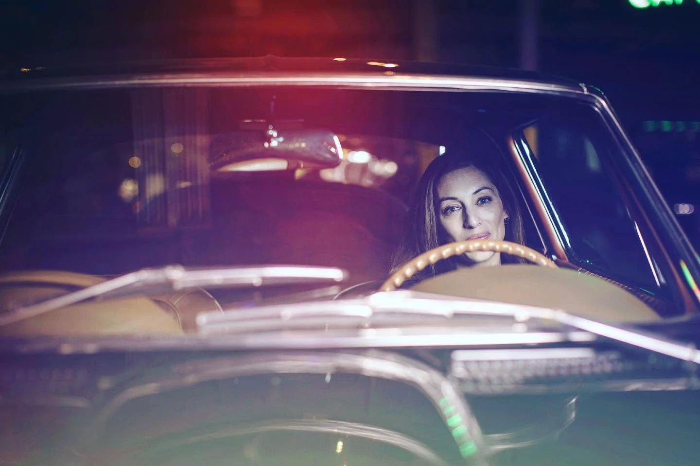 Cinematic portrait of woman driving vintage car at night.