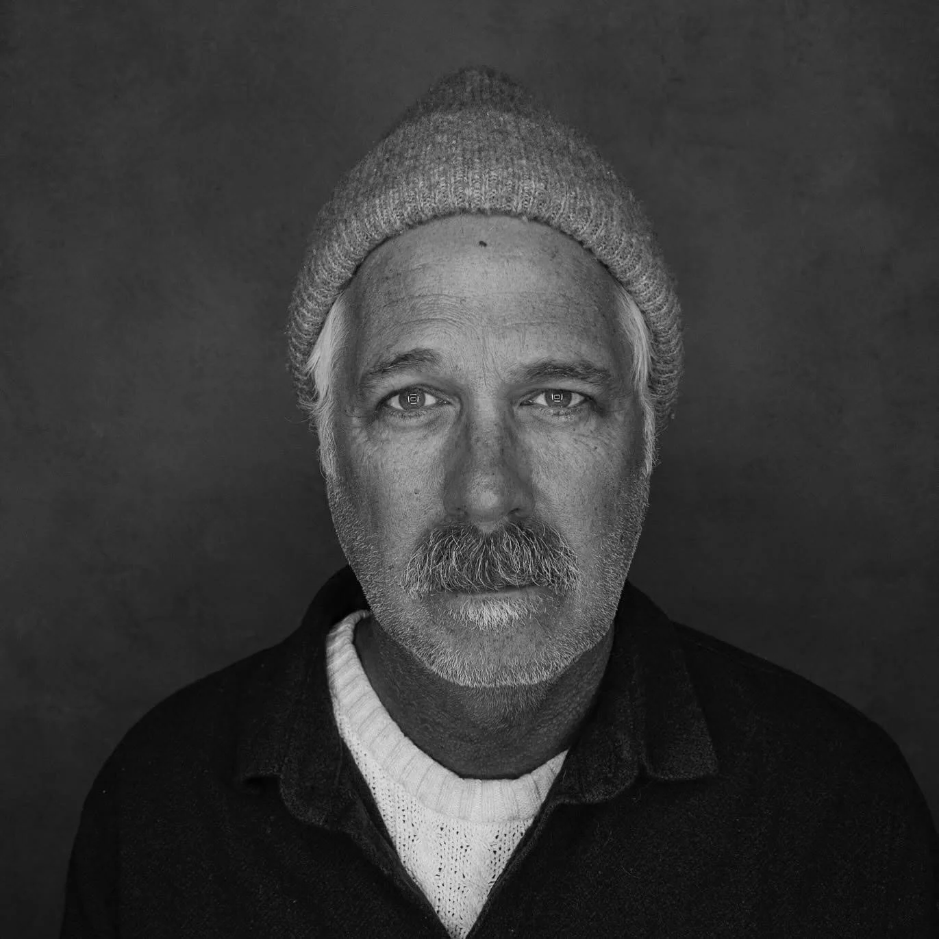 Black and white studio portrait of Michael Poehlman wearing a knit cap.