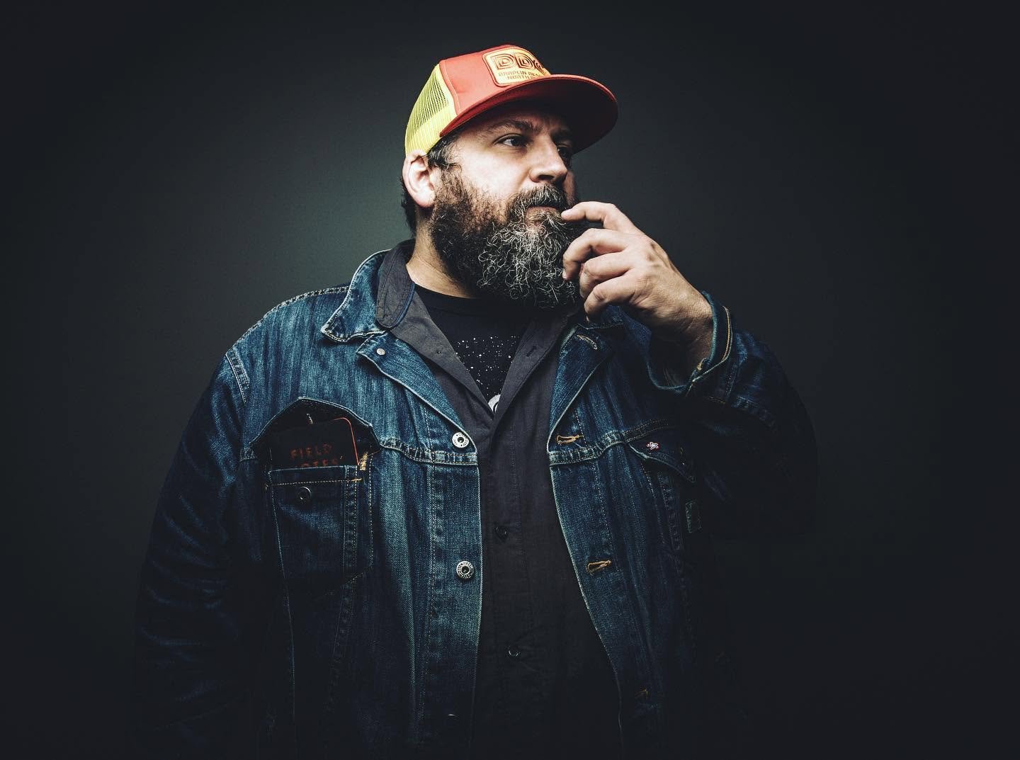 Editorial portrait of Aaron Draplin wearing denim jacket and cap.