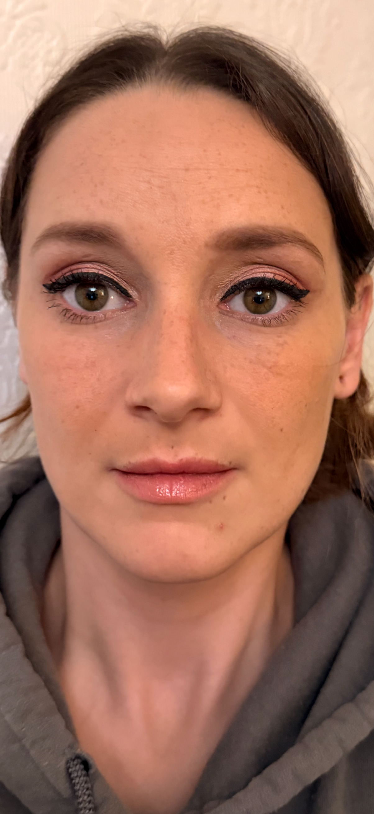 Close-up of a young, wearing makeup with pink eyeshadow, black eyeliner, and shiny lipstick