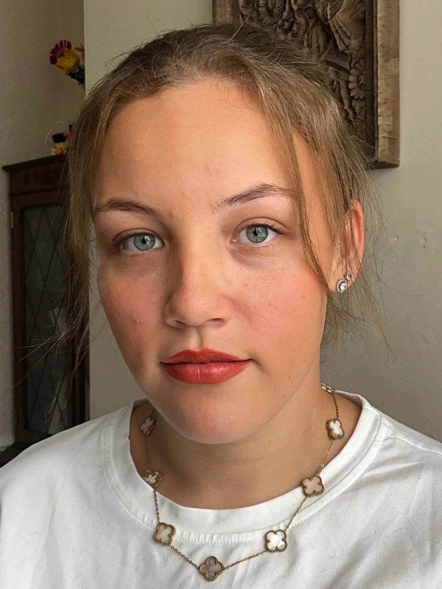 Close-up of a young woman with light skin, blue eyes, wearing red lipstick, with a natural makeup look