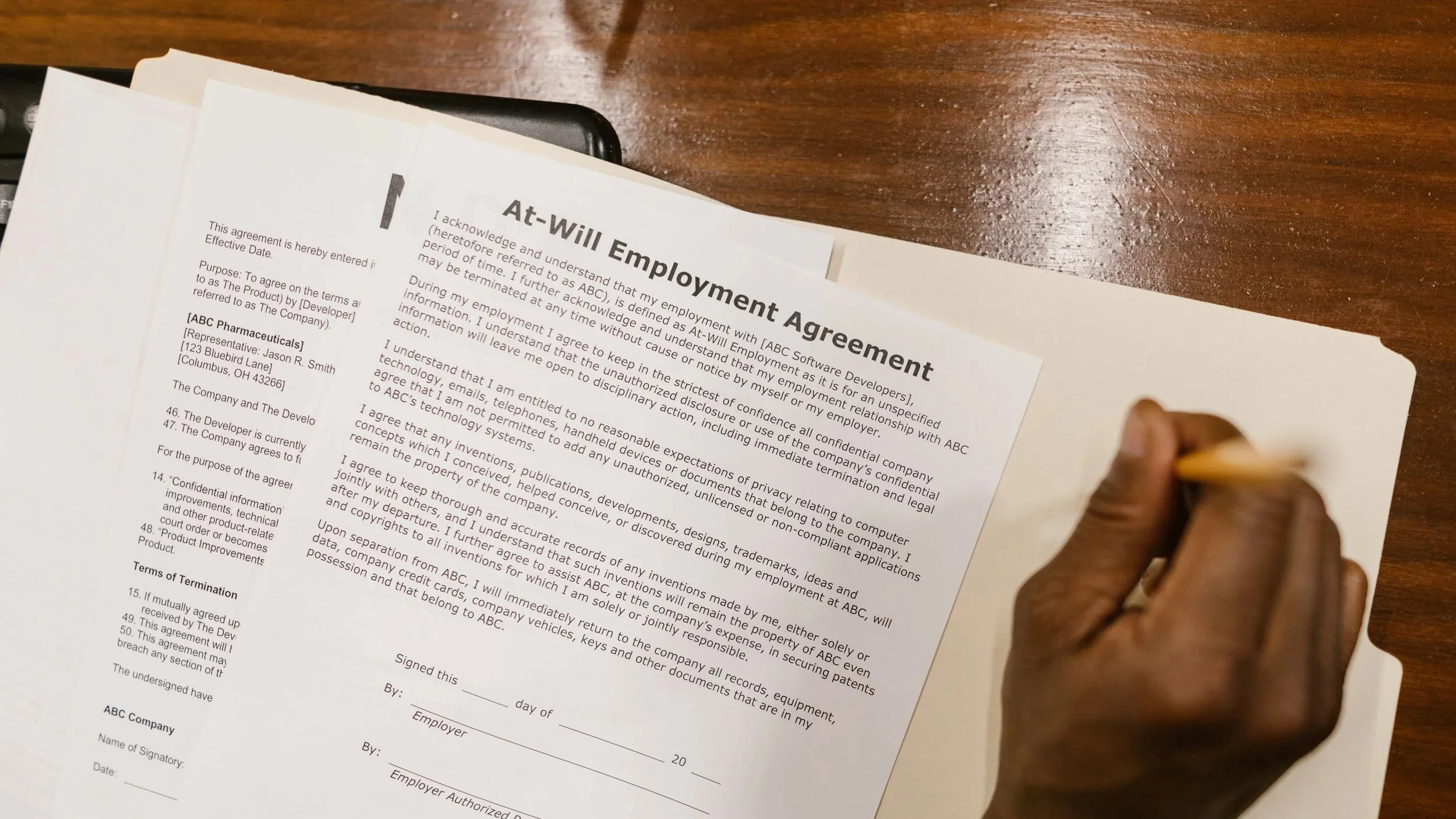 Person signing an employment agreement document on a wooden table.