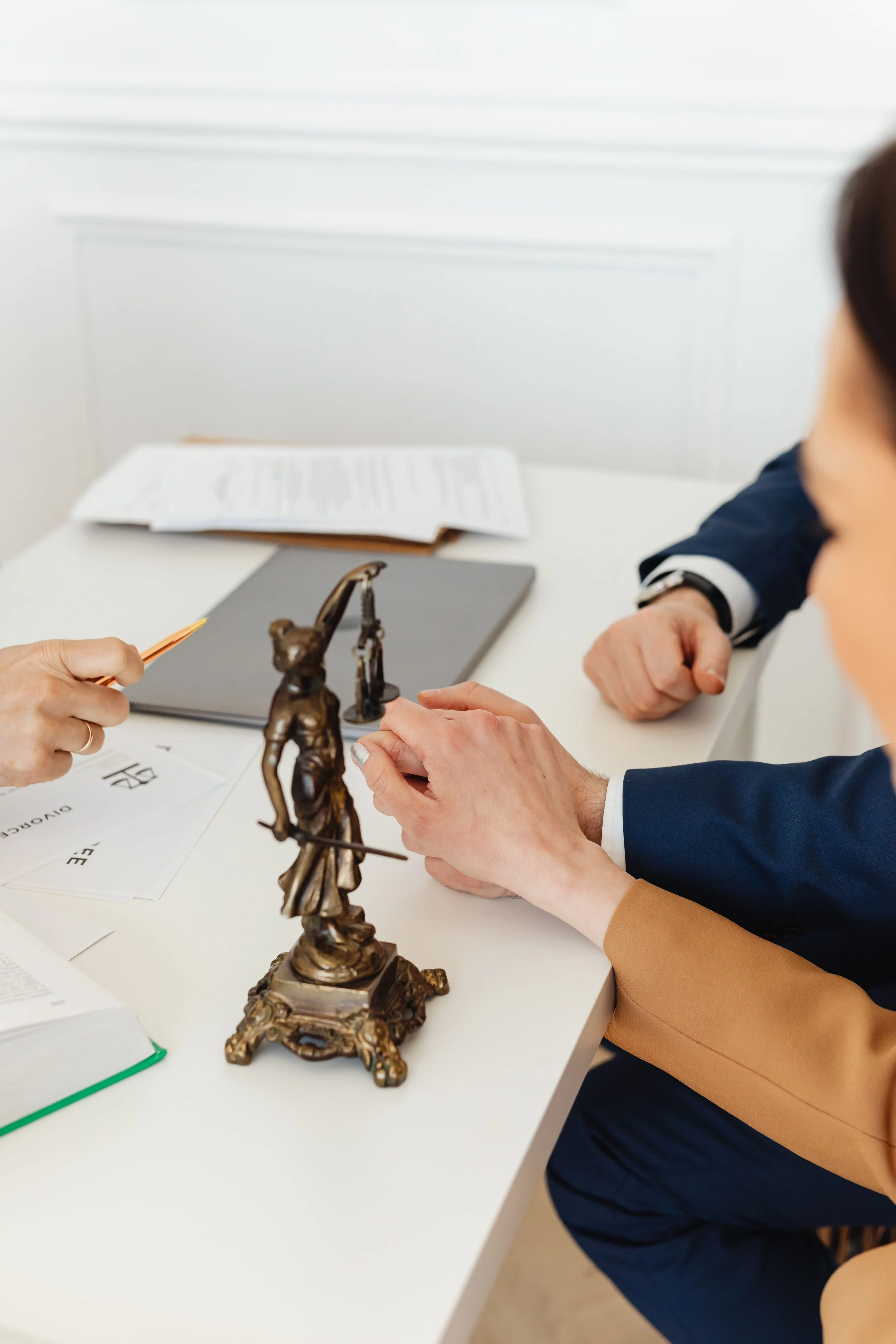 People sitting at a table during a meeting or discussion, with documents, a small statue of Lady Justice, and a metal sculpture of a judge on the table.