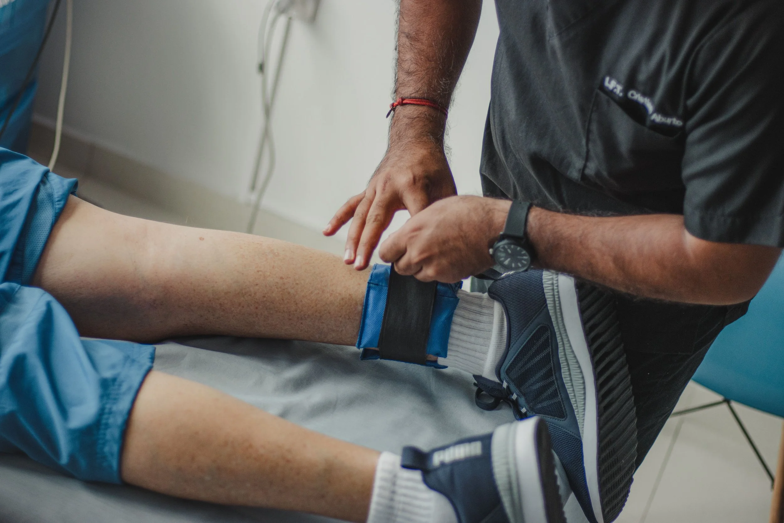 A healthcare professional examining a patient's leg, which is positioned on an examination table in a clinic or hospital setting.