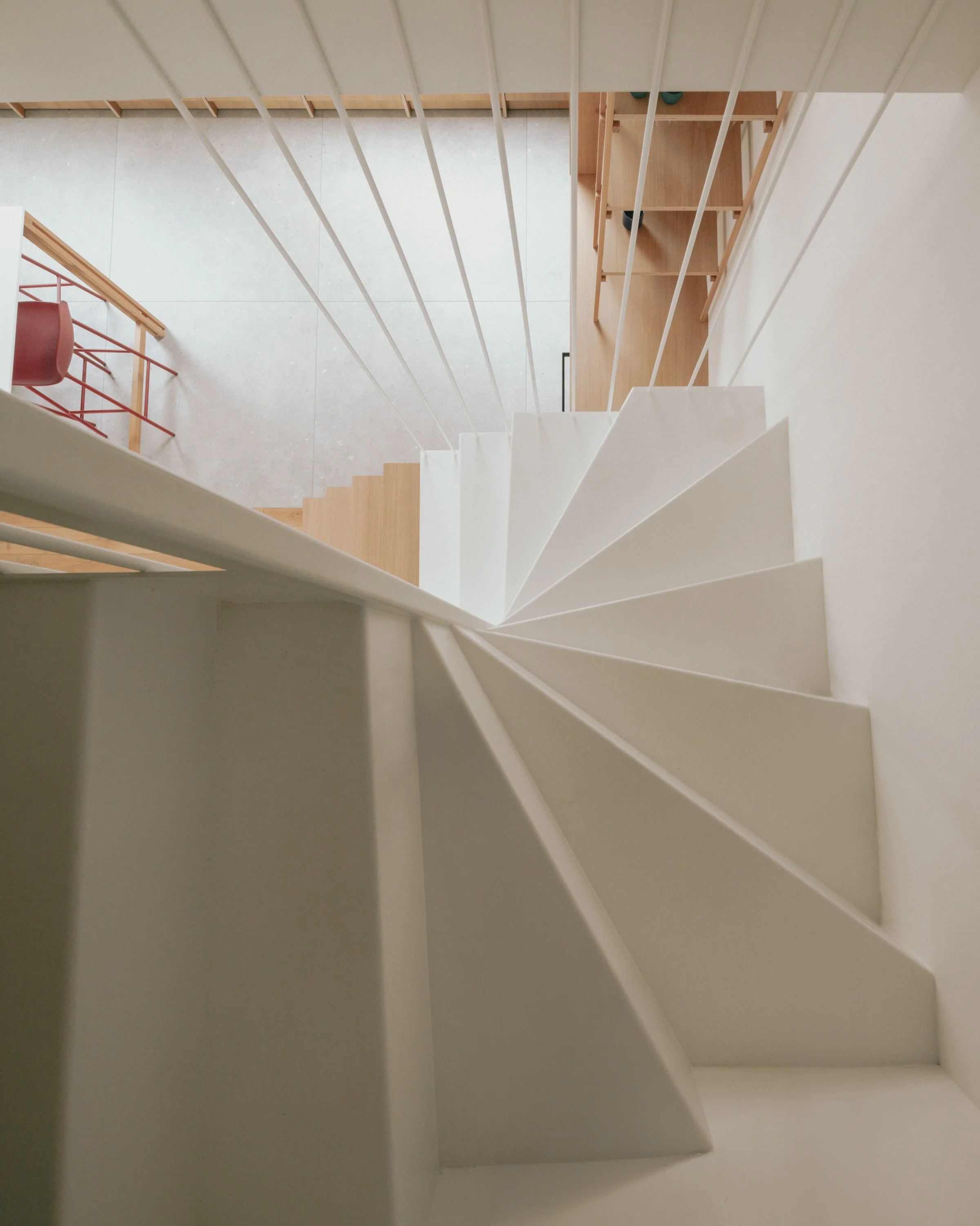 Vue du dessus d'un escalier en colimaçon blanc avec des rampes blanches, vue de haut vers le bas, avec un sol en carrelage clair et un mobilier en bois visible dans l'espace en dessous.