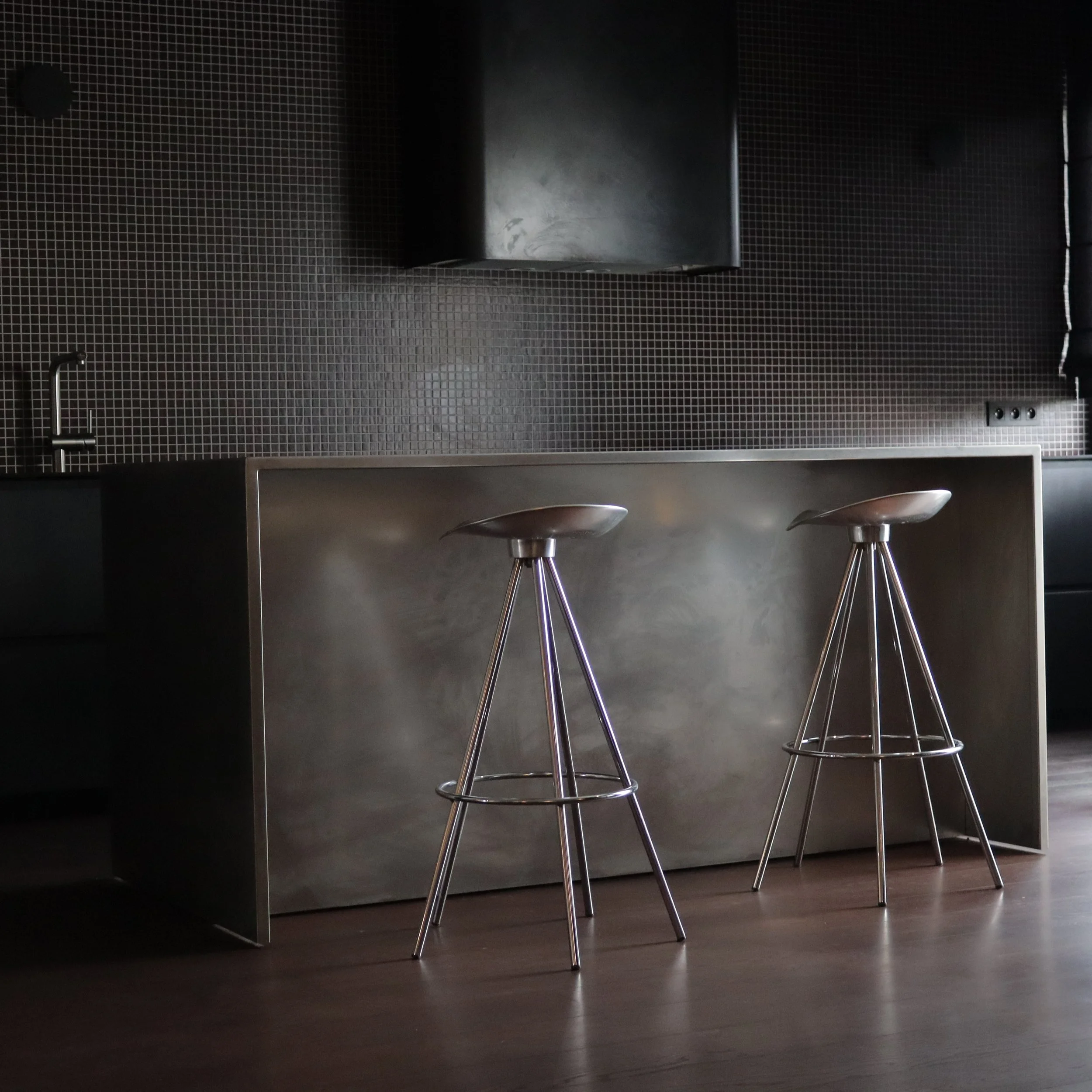 Deux tabourets en acier inoxydable devant un comptoir noir dans une cuisine moderne.