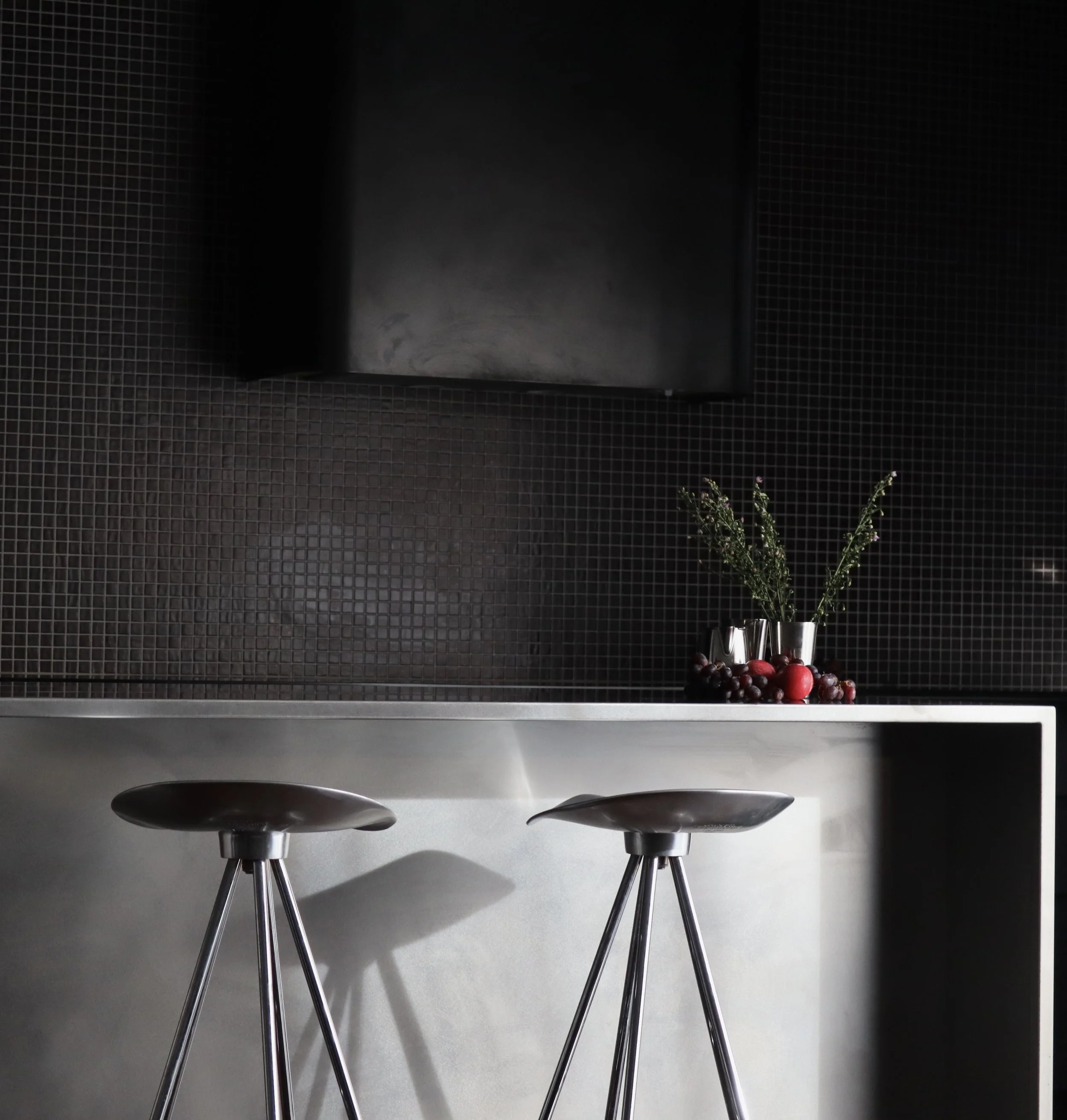 Table en métal avec deux chaises modernes en face, décorée avec un vase contenant des branches vertes, dans une pièce au mur noir avec carrelage.