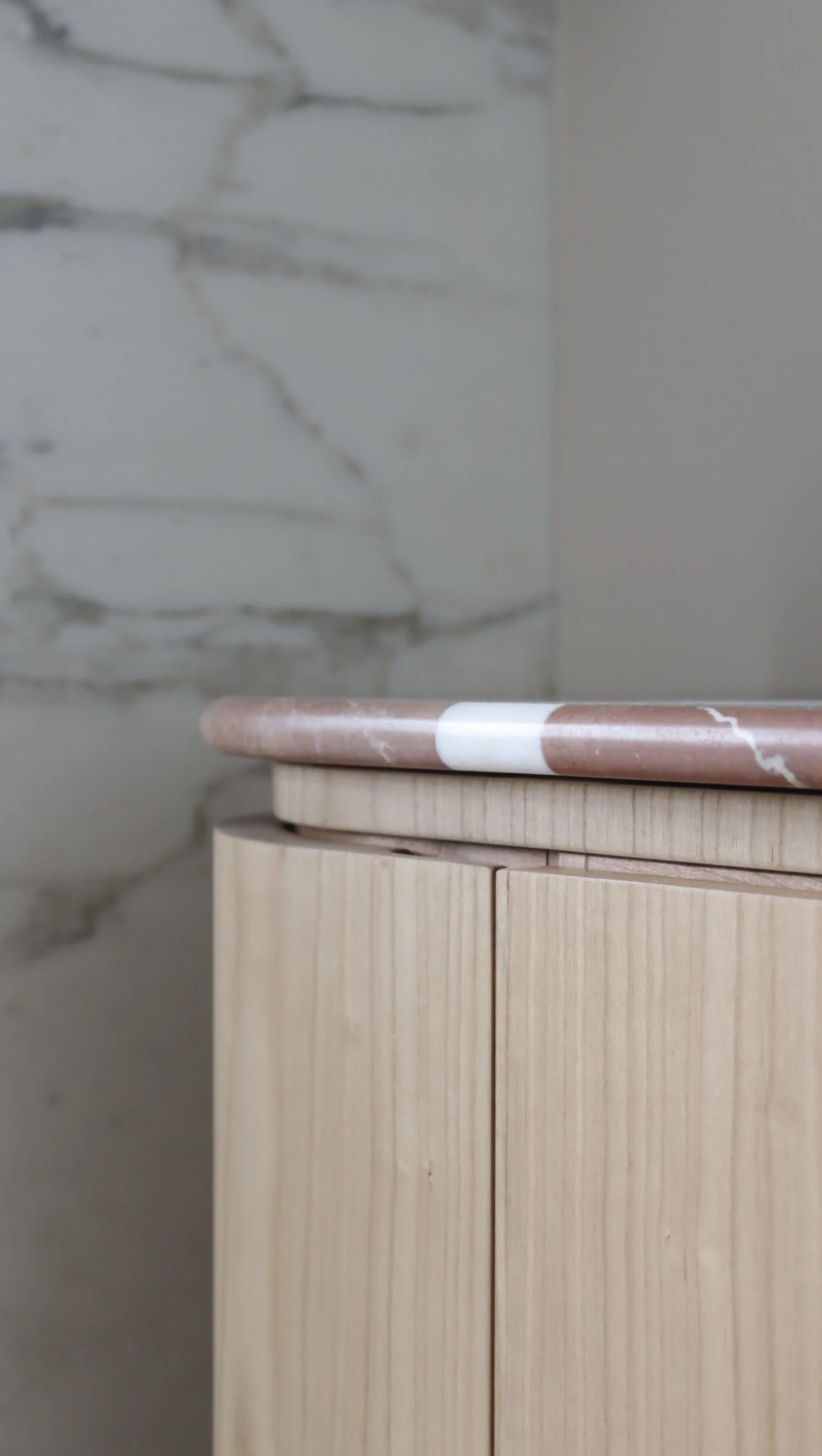 Deux plateaux posés l'un sur l'autre, avec le fond d'une cloison en plâtre. Le plateau supérieur est en marbre rose avec des veines blanches, le plateau inférieur est en bois clair.