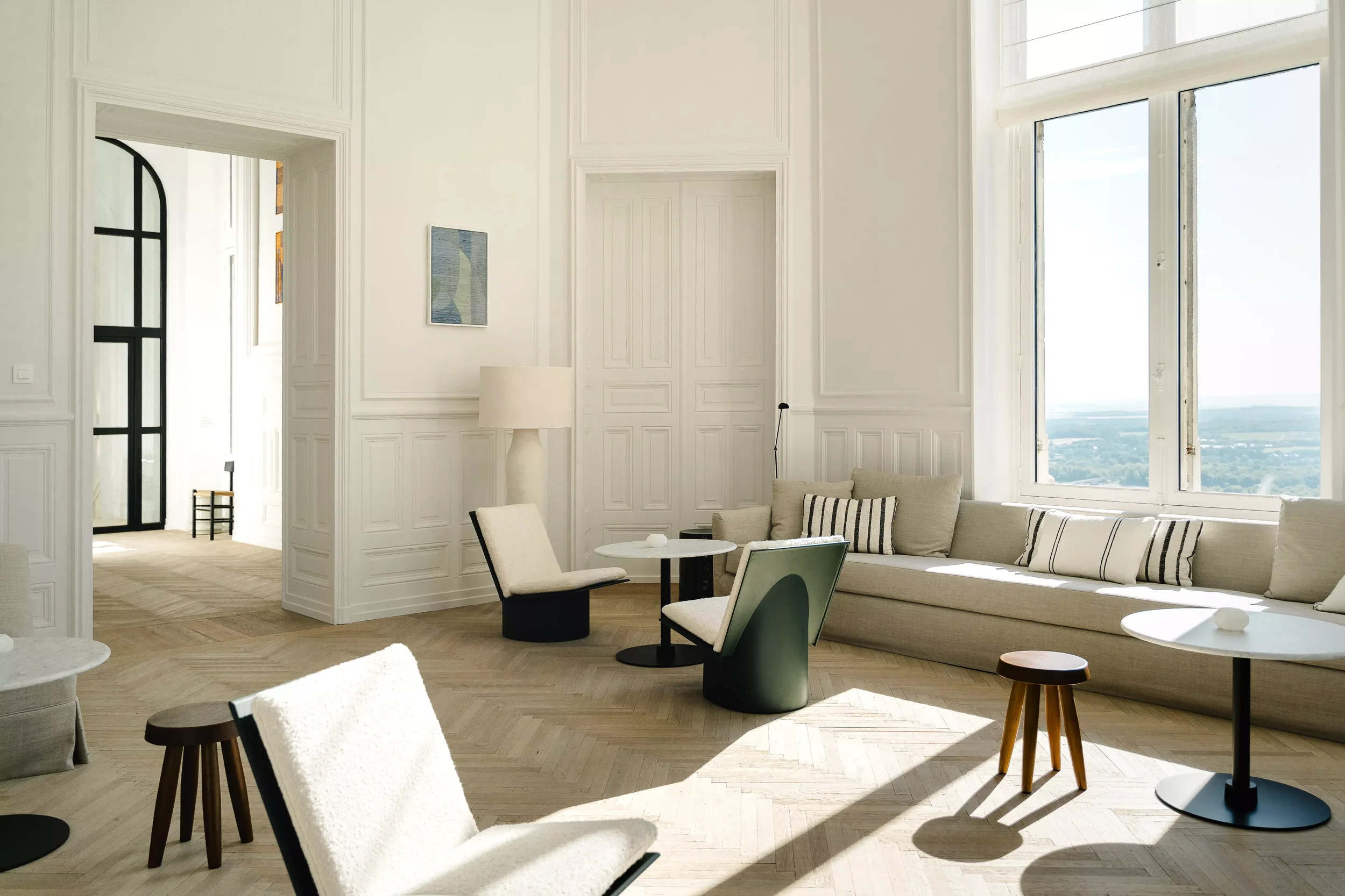Salon lumineux avec grands fenêtres, canapé beige, et mobilier moderne.